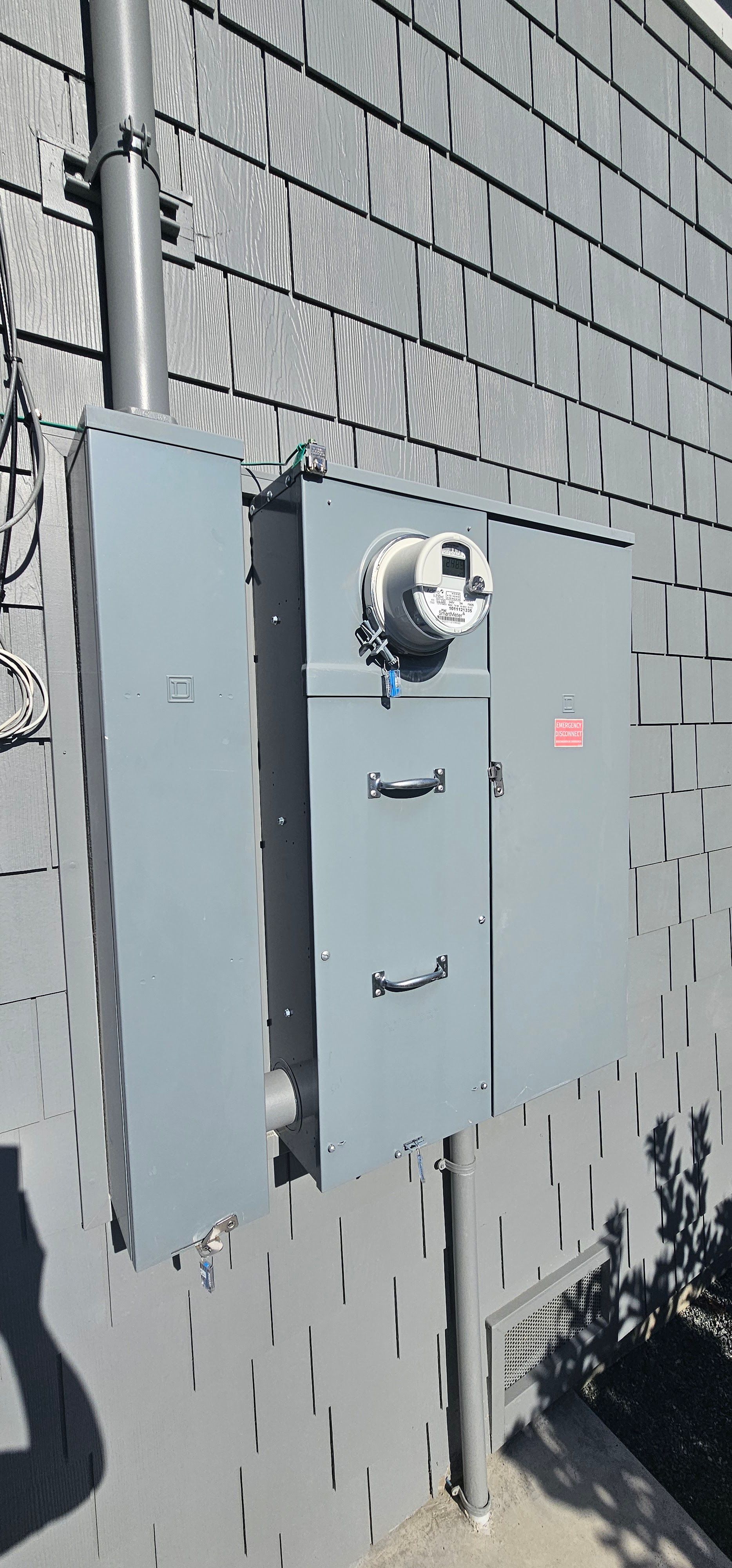 Gray utility electrical panels mounted on a brick wall outdoors, with a meter and conduit