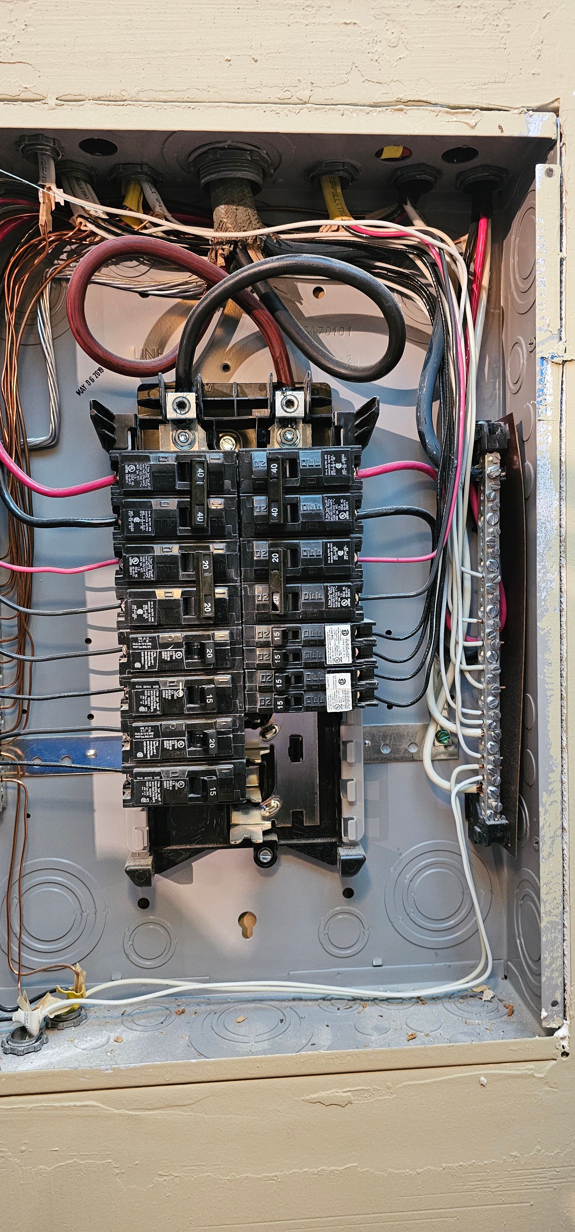 Open electrical breaker panel with multiple switches and exposed wiring in a wall recess