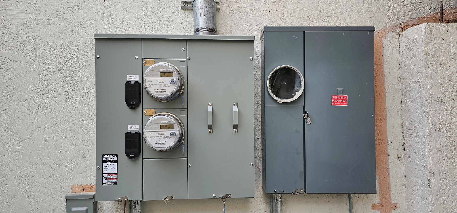 Two gray utility meter boxes mounted on a stucco wall, with round meters and conduit