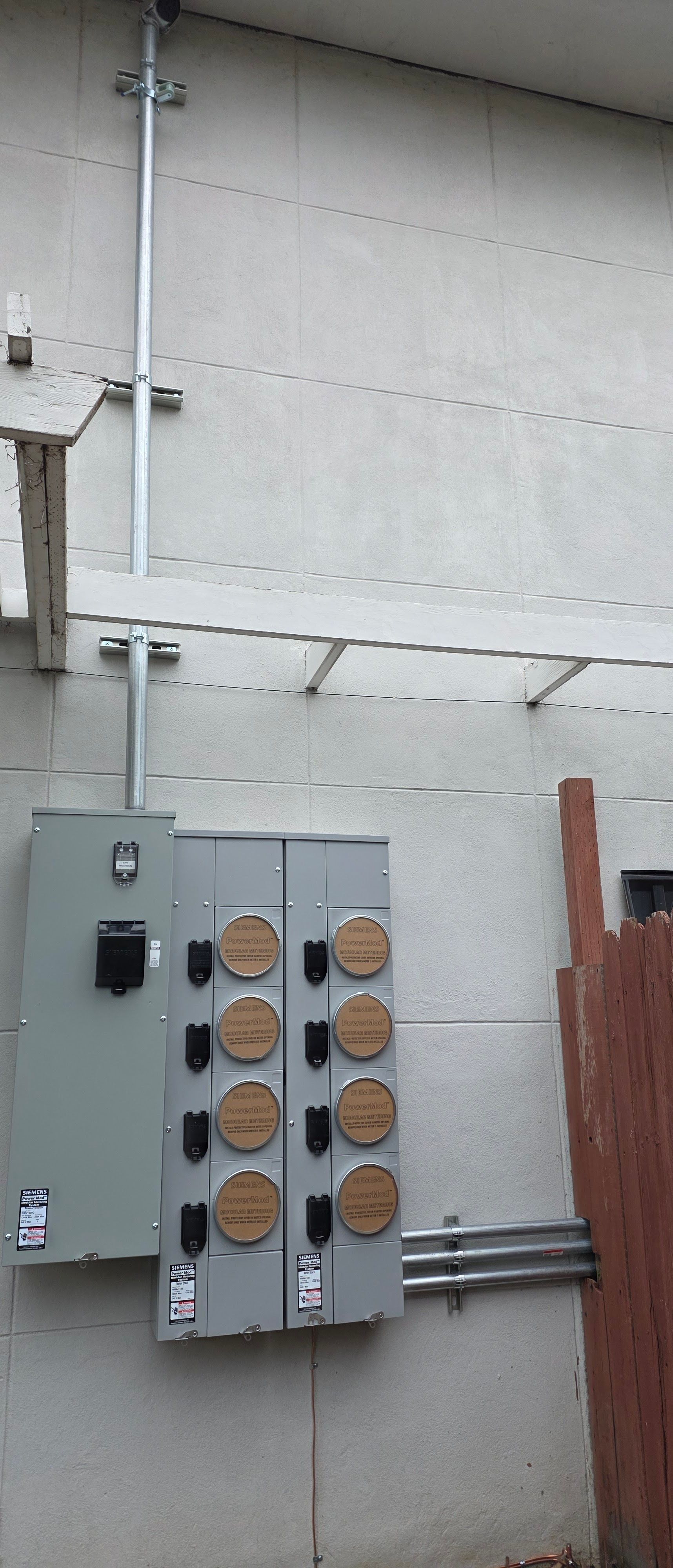 Outdoor wall with electrical panels, conduit, and a utility meter cluster.
