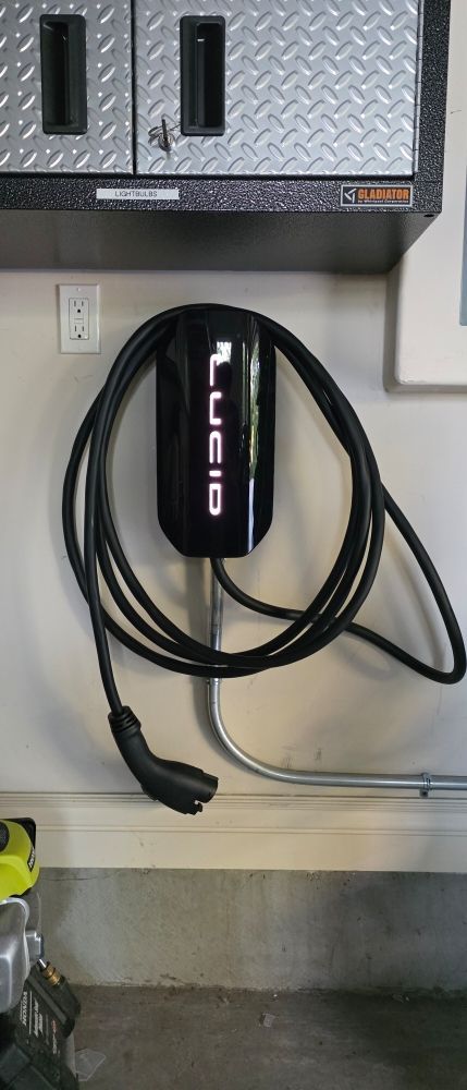 Wall-mounted EV charger with coiled black cable beneath a gray cabinet in a garage or utility area