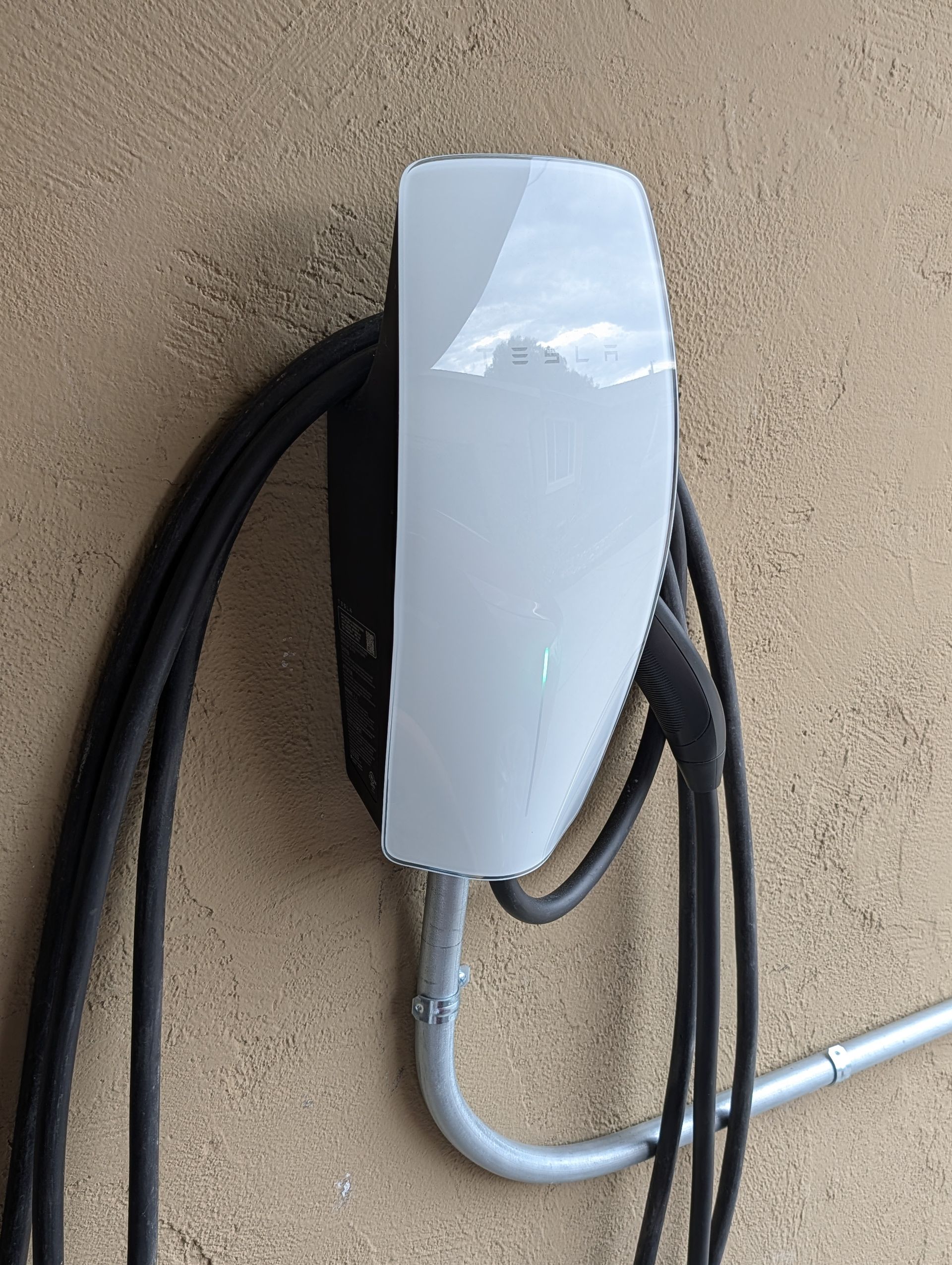 White wall-mounted EV charger with black and gray cables on a textured beige wall.