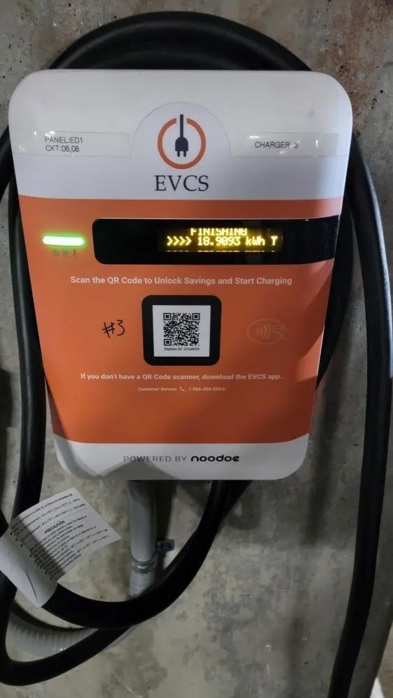 Wall-mounted EV charging station with orange and white panel, QR code, and coiled cable