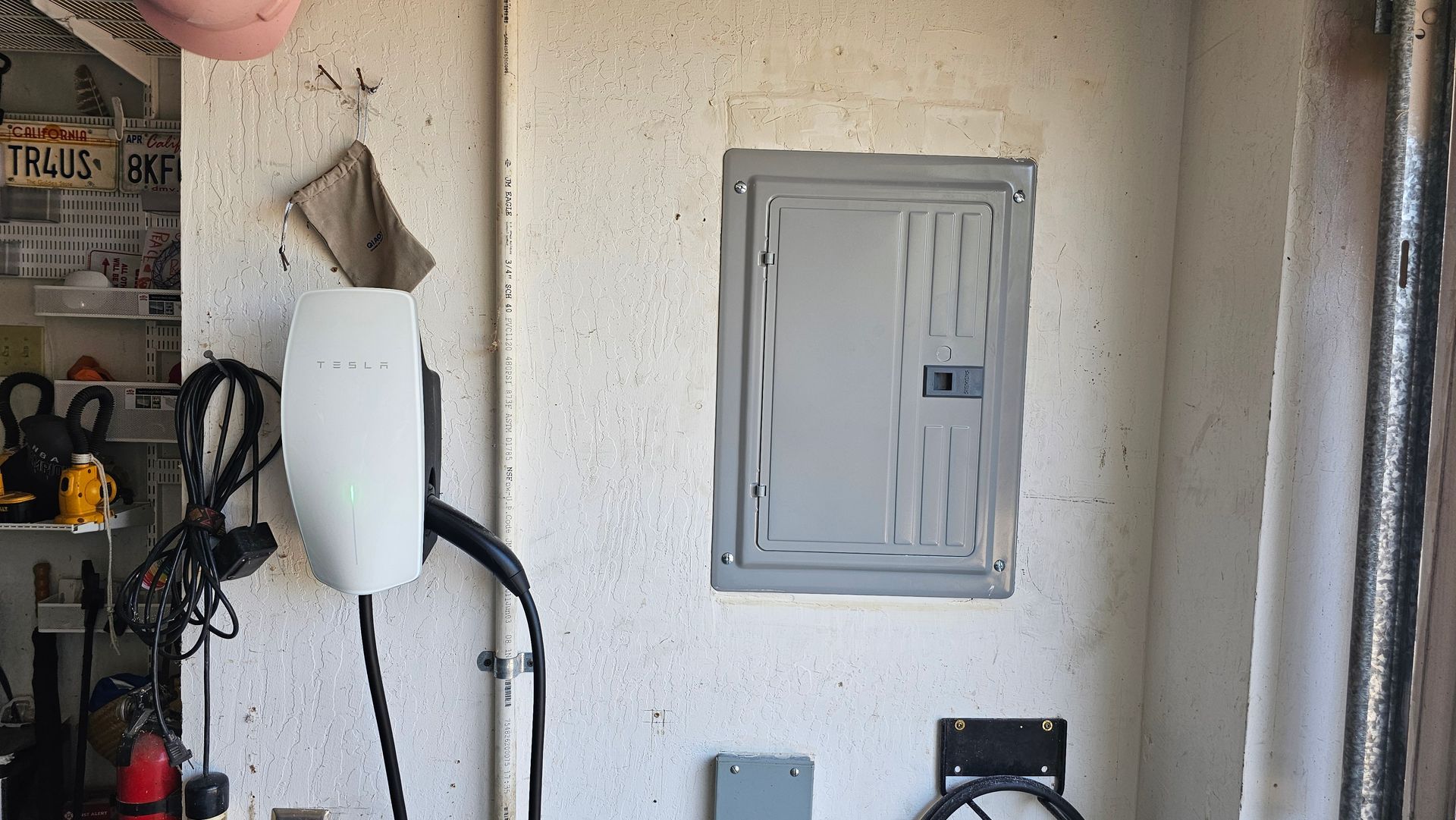 Utility room wall with gray electrical panel, white tank, and tools on shelves.