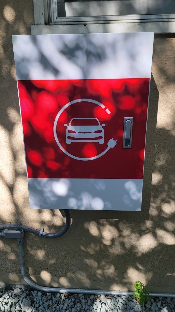 Red and white EV charging station mounted on an outdoor wall in dappled sunlight