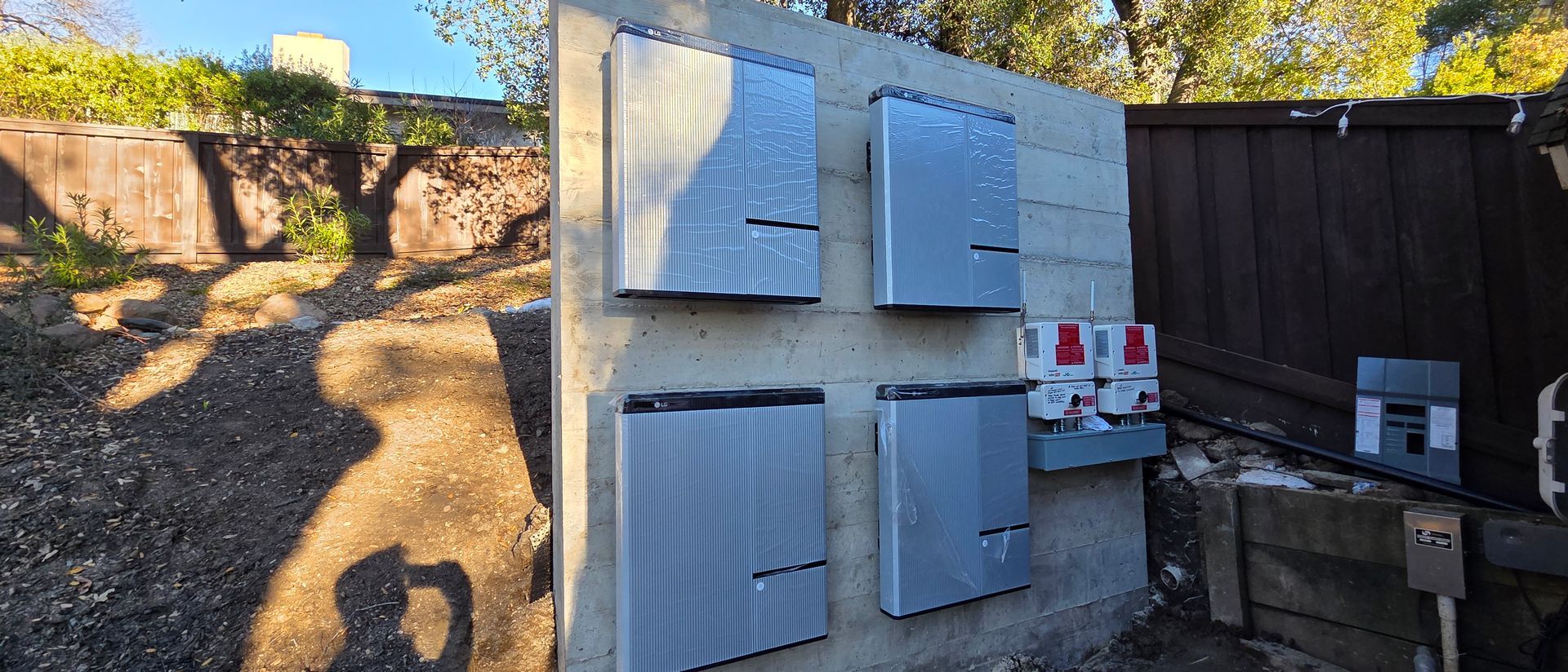 White utility boxes mounted on a fence in a sunlit backyard