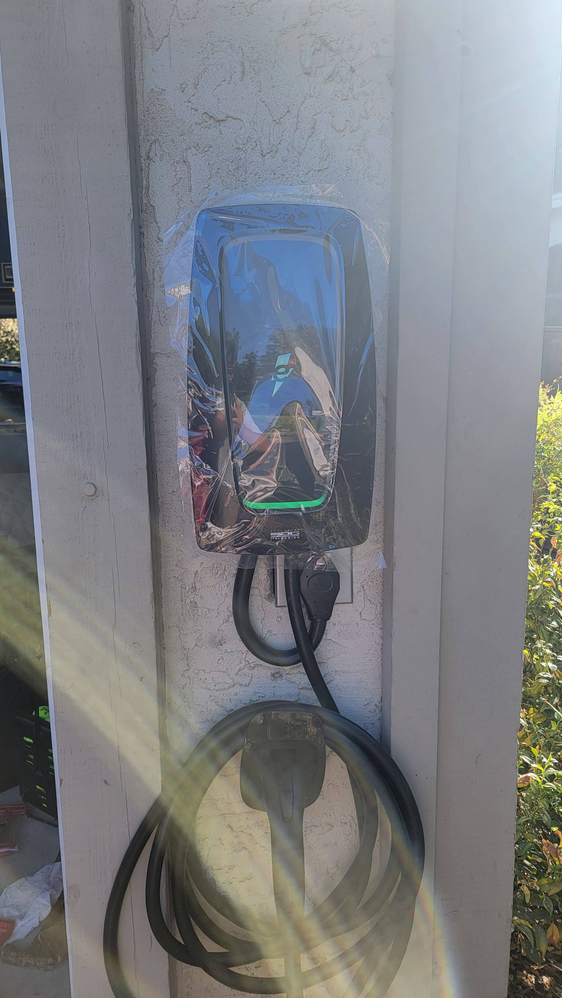 Outdoor wall-mounted electrical outlet with a plugged-in black cord and coiled cable hanging below