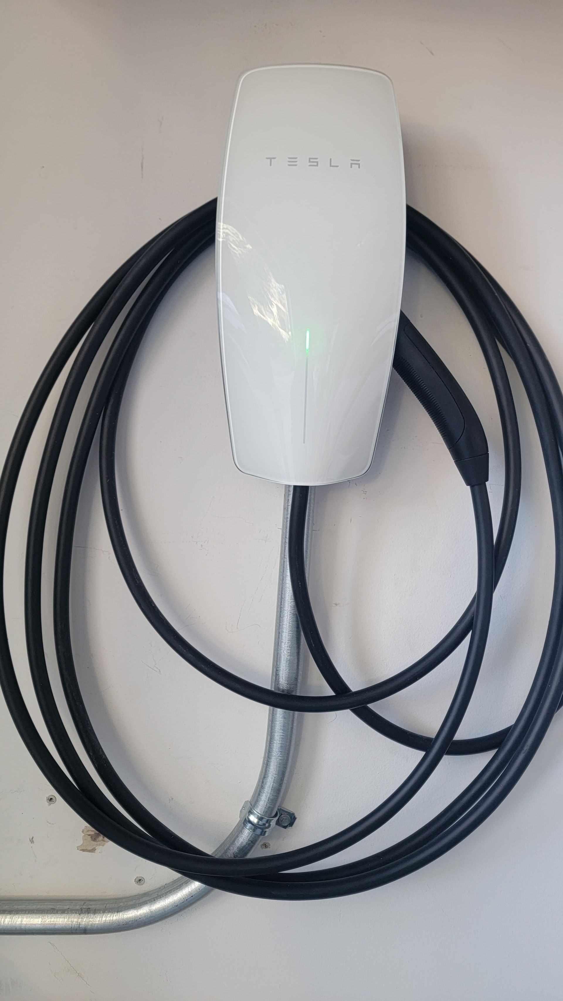 White wall-mounted EV charger with a coiled black cable on a light wall