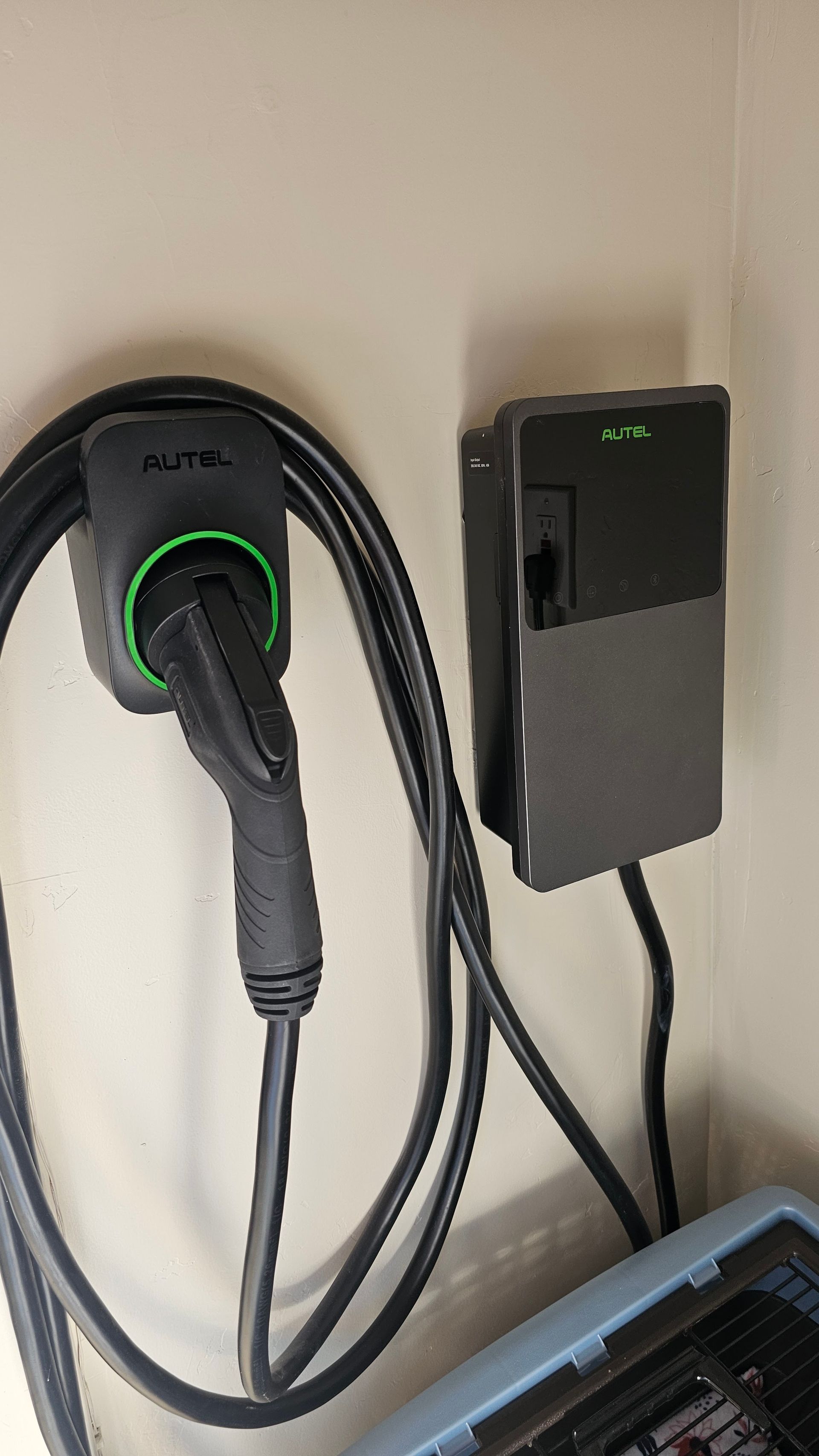 Wall-mounted Tesla charger with coiled cable and black charging box beside it