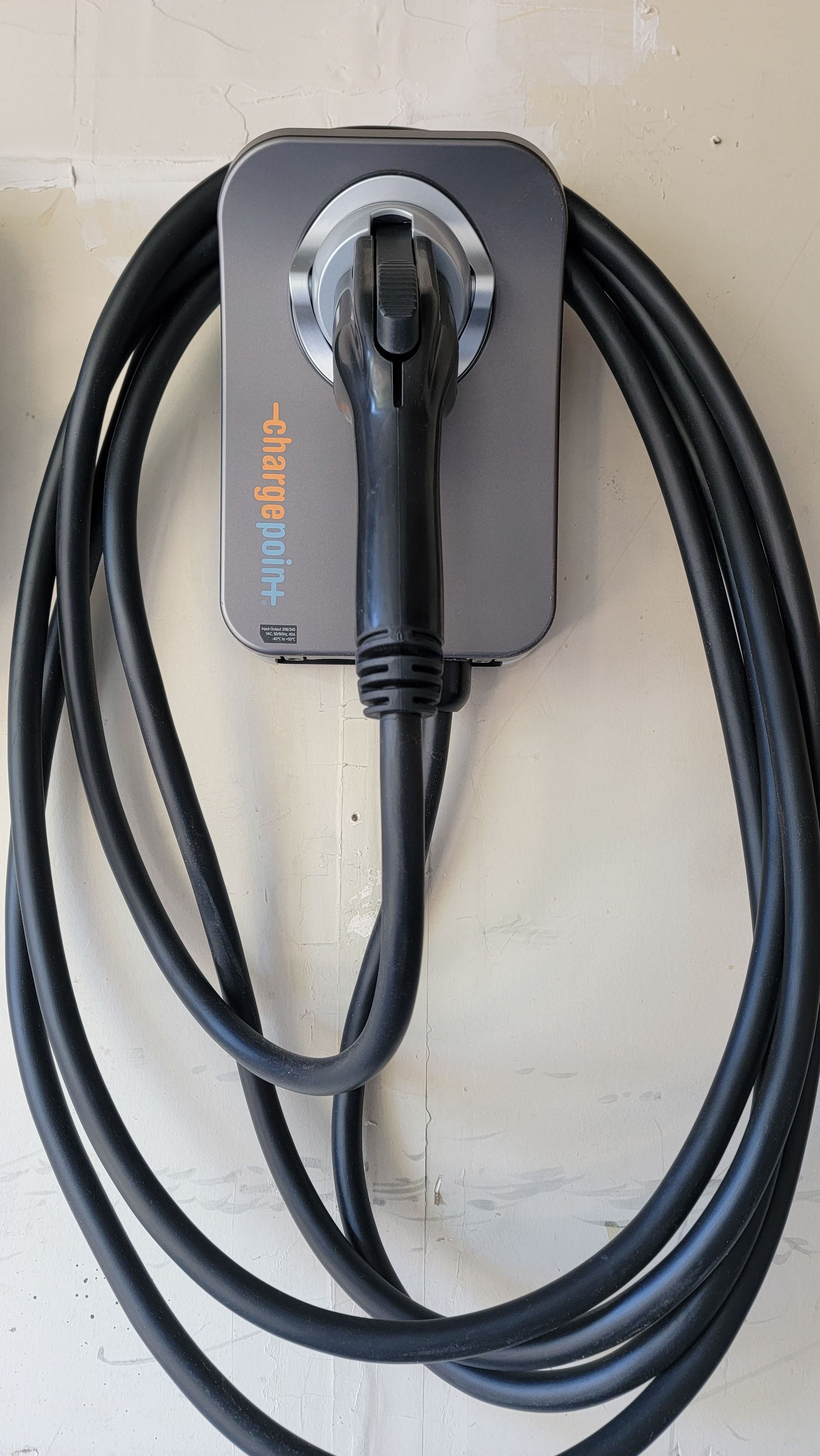 Black EV charging cable coiled around a gray wall-mounted charger unit.