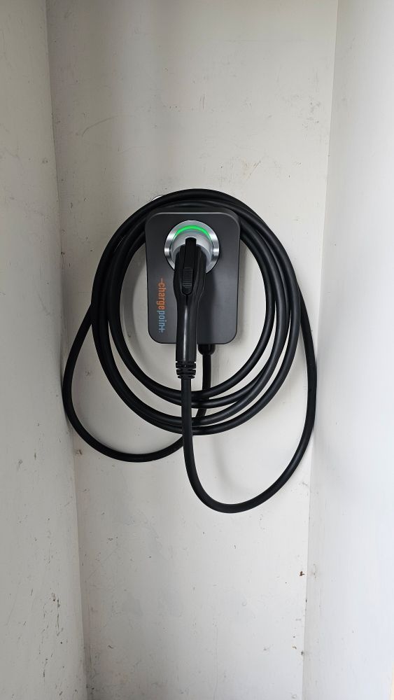 Black EV charging cable coiled on a wall-mounted charger against a white wall