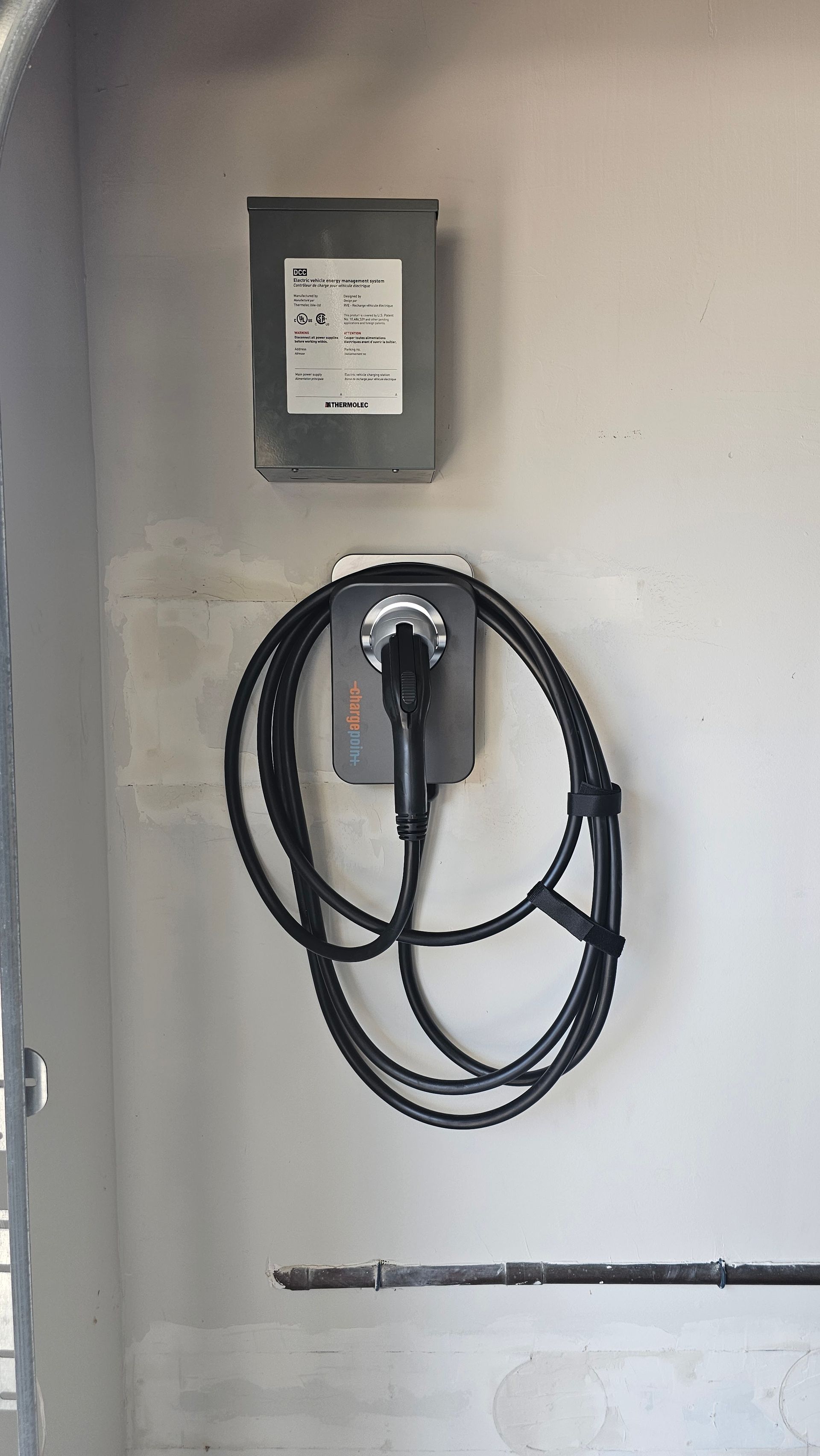 Wall-mounted electric vehicle charging station with a coiled black cable and connector on a white wall.