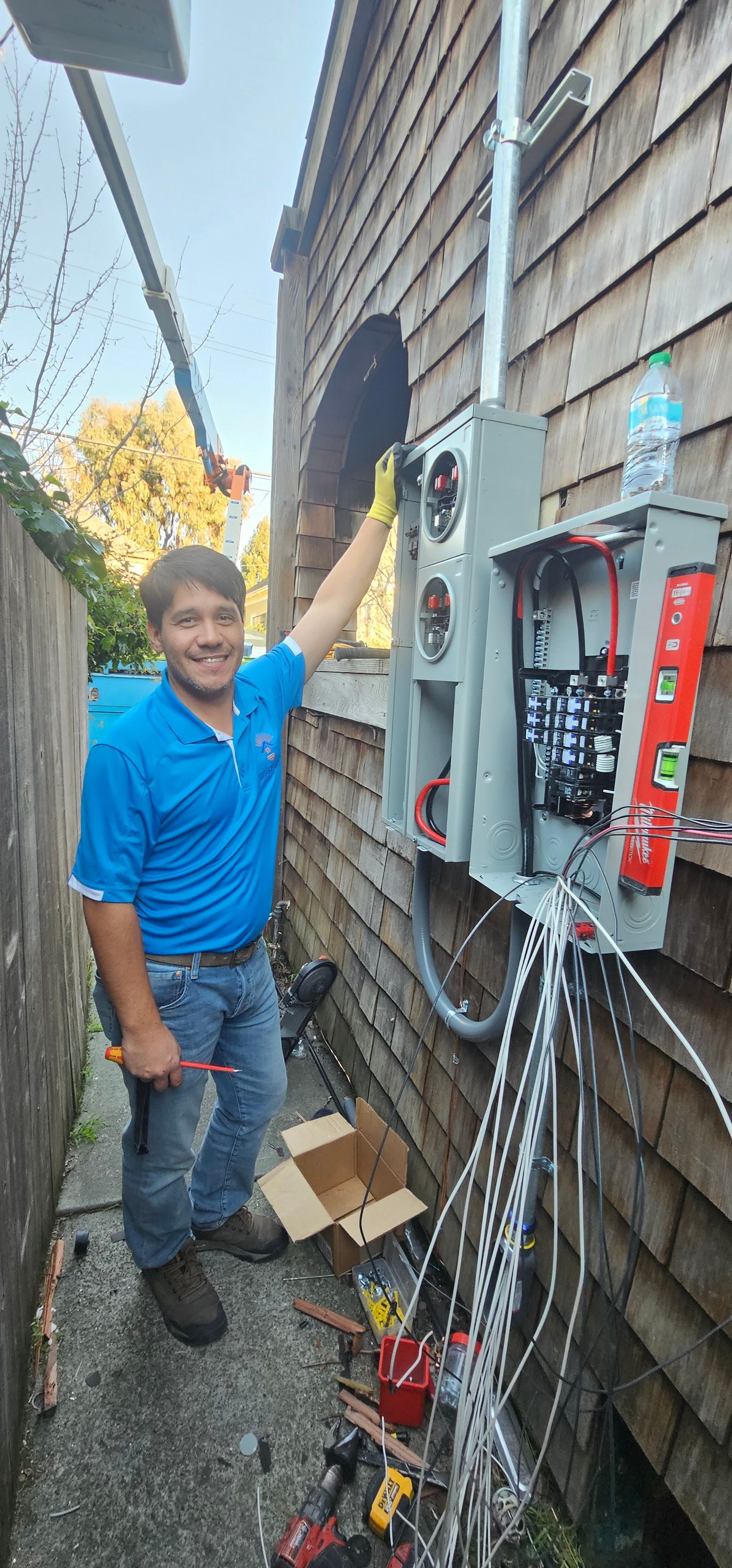 Technician adjusting an outdoor electrical panel on the side of a house, with wires and tools nearby.