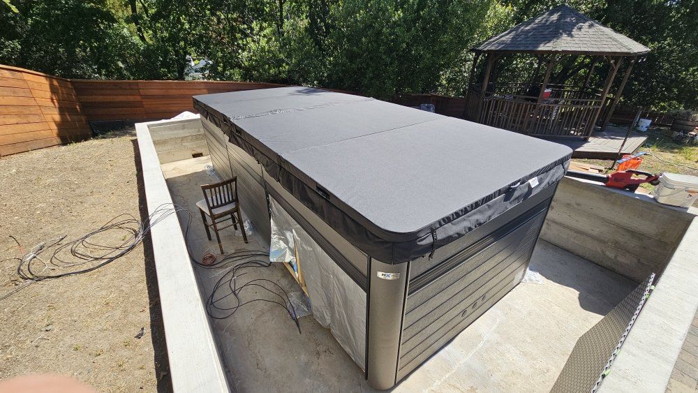 Outdoor patio with a large gray hot tub or spa surrounded by concrete walls and trees