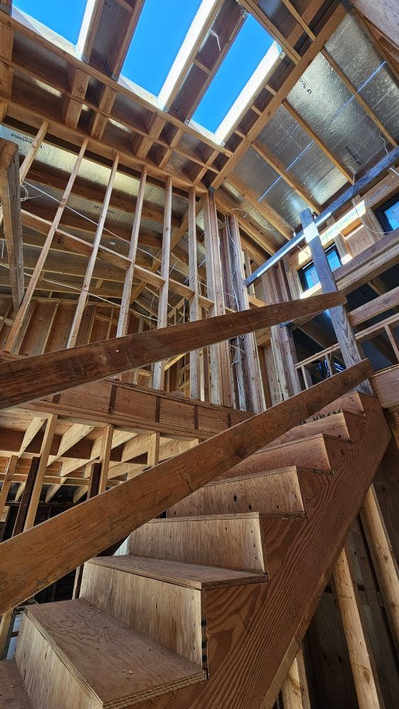 Unfinished wooden staircase inside a framed building under construction, with exposed beams and skylights.
