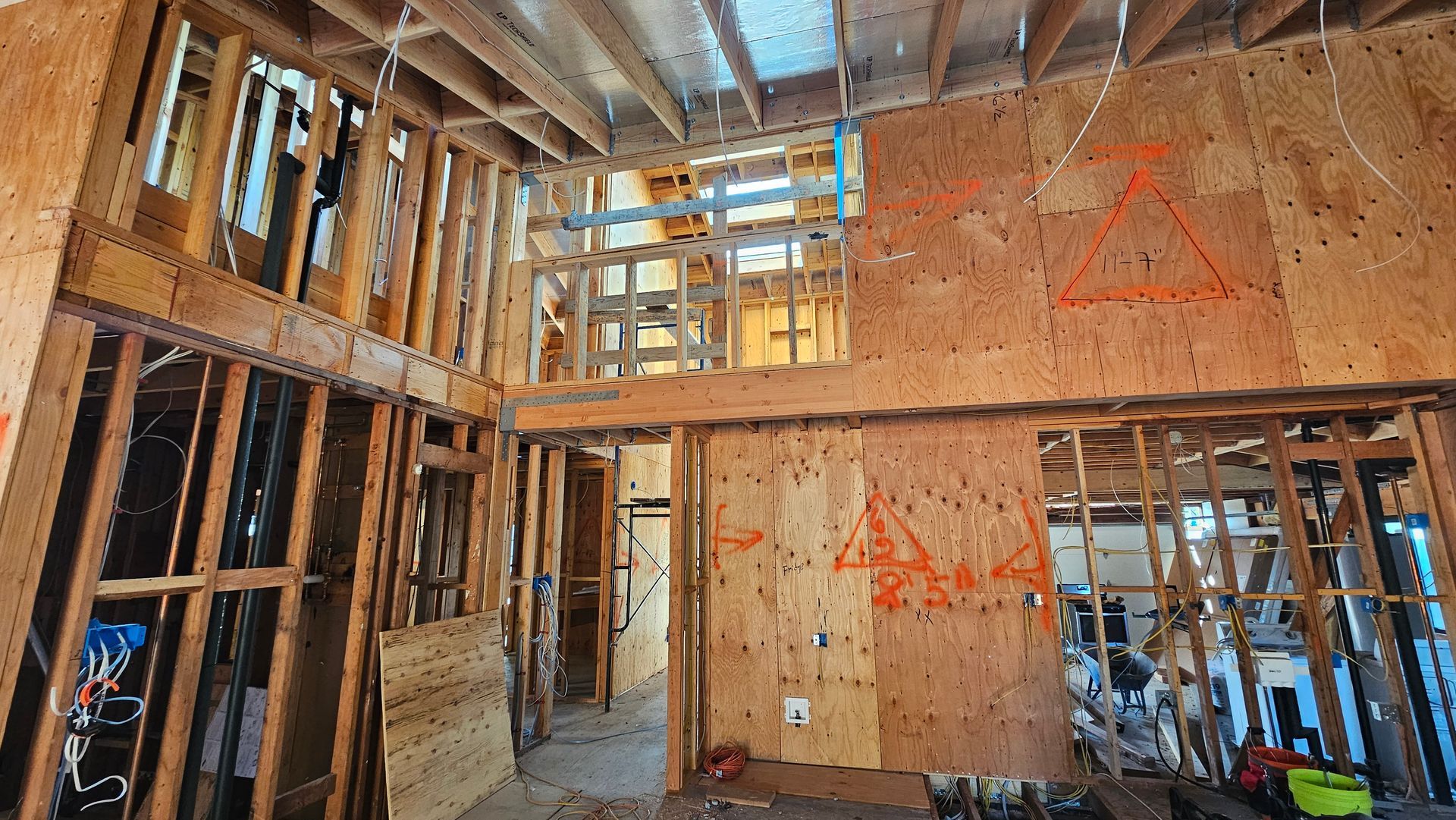 Interior of a house under construction, with exposed wood framing, plywood walls, and scaffolding.