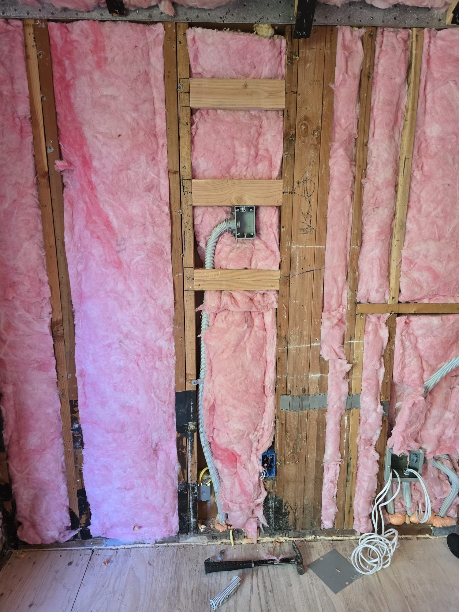 Pink fiberglass insulation between exposed wooden wall studs in an unfinished interior wall.