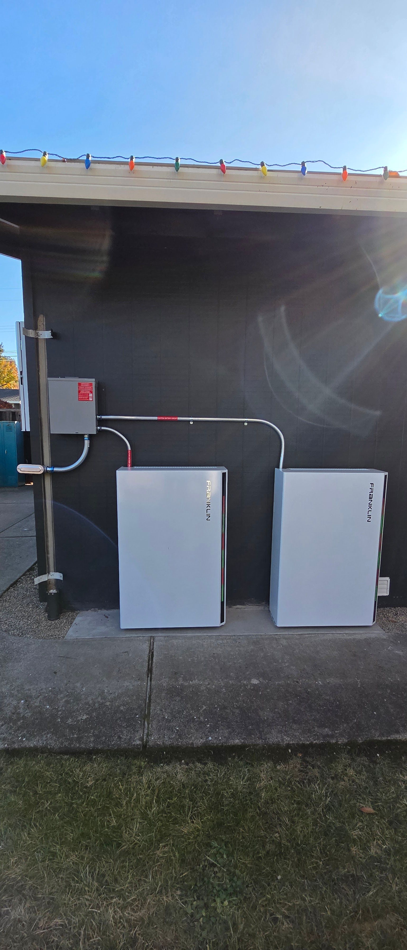 Two white utility boxes with conduits under a roof overhang beside a building
