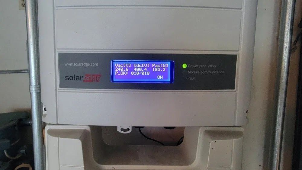 Wall-mounted solar inverter with blue LCD display and green status light in a metal frame