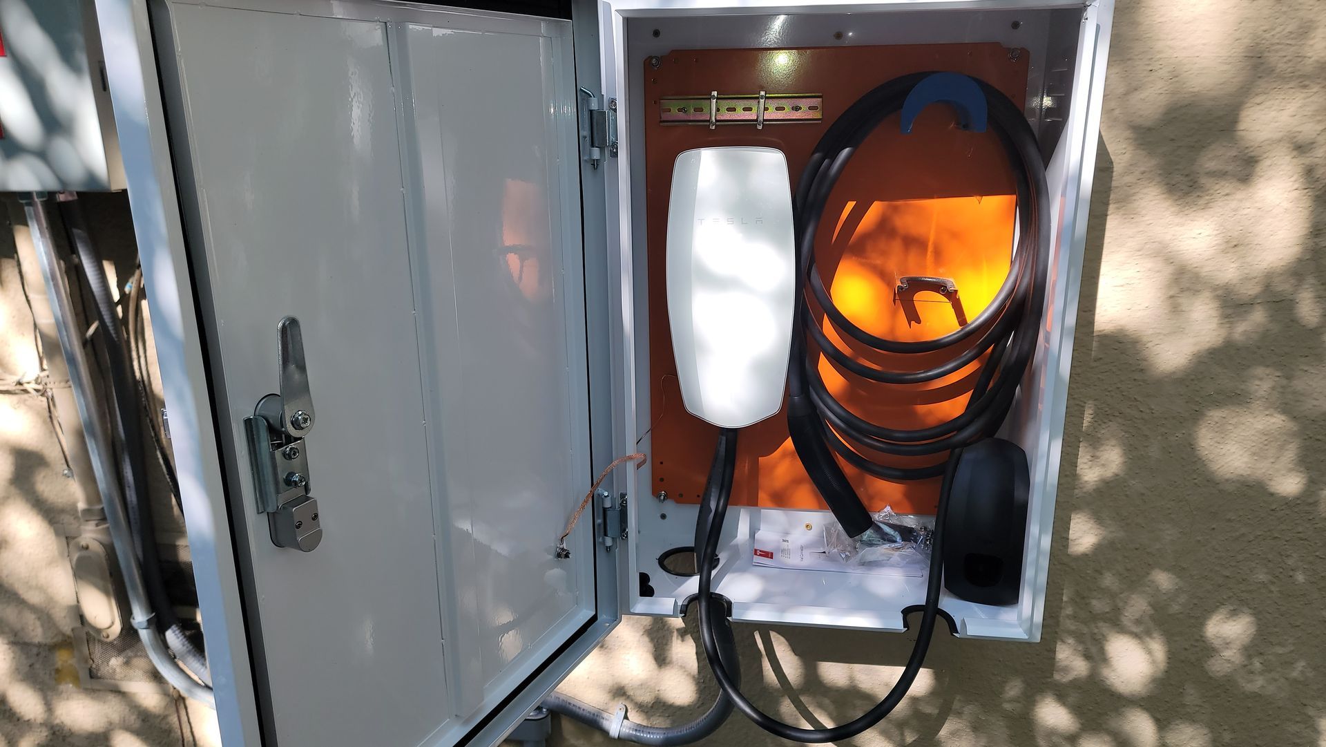 Open electrical panel with orange safety gear hanging inside and a white cloth on the door