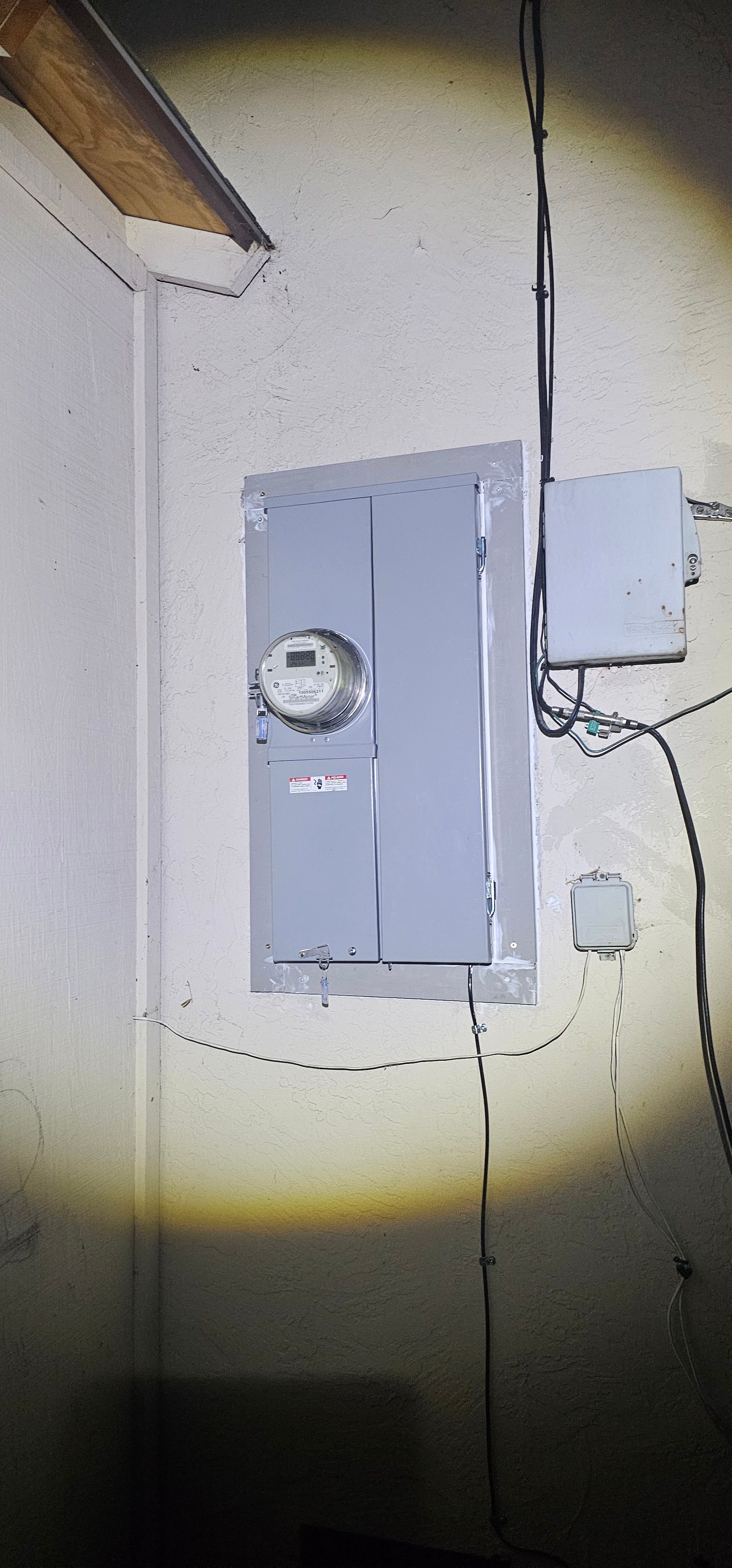 Electrical meter and breaker panel on a wall, lit by a flashlight beam.