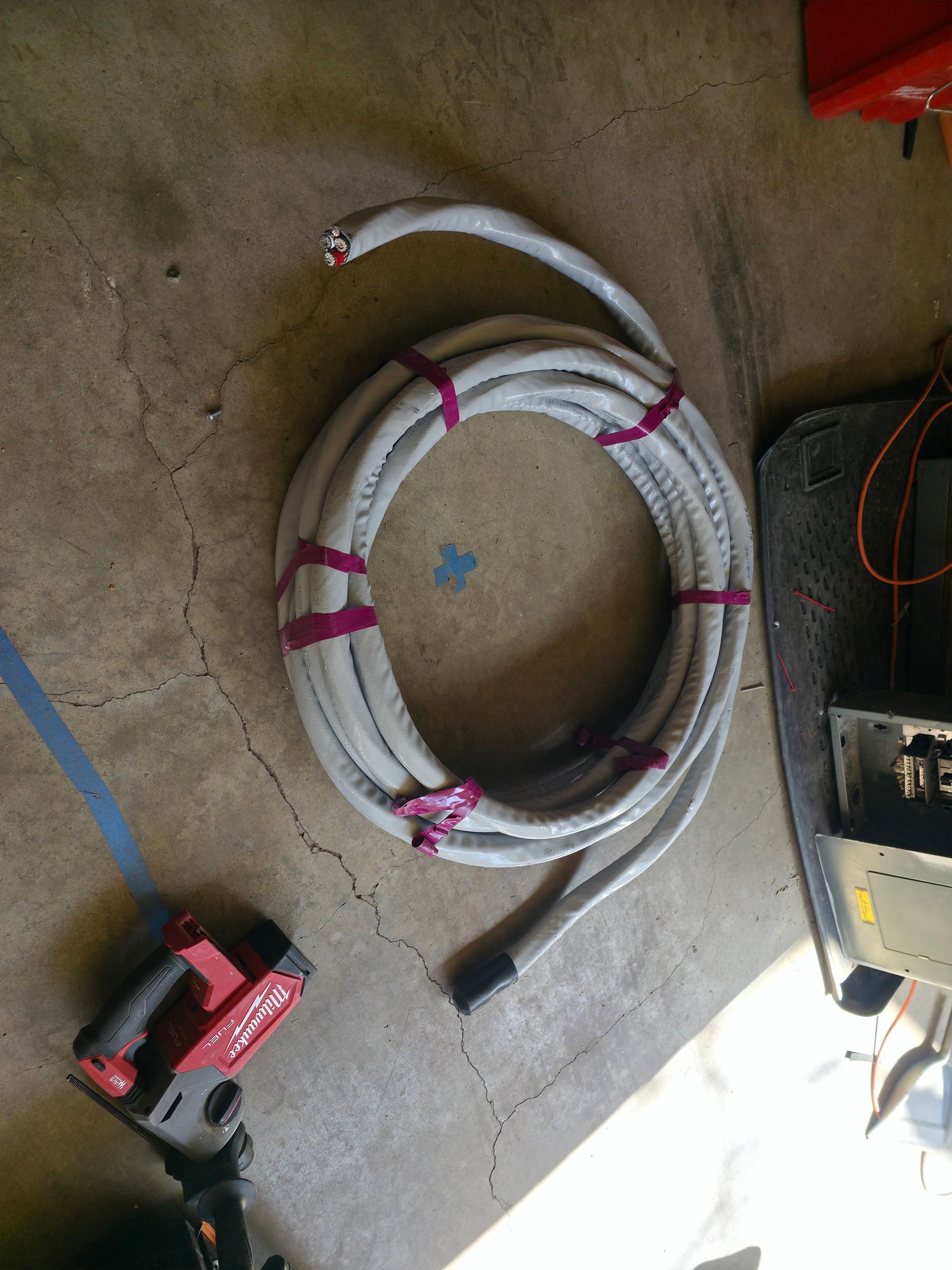 Coiled white hose on concrete floor with pink ties, next to a red cordless drill and tools.