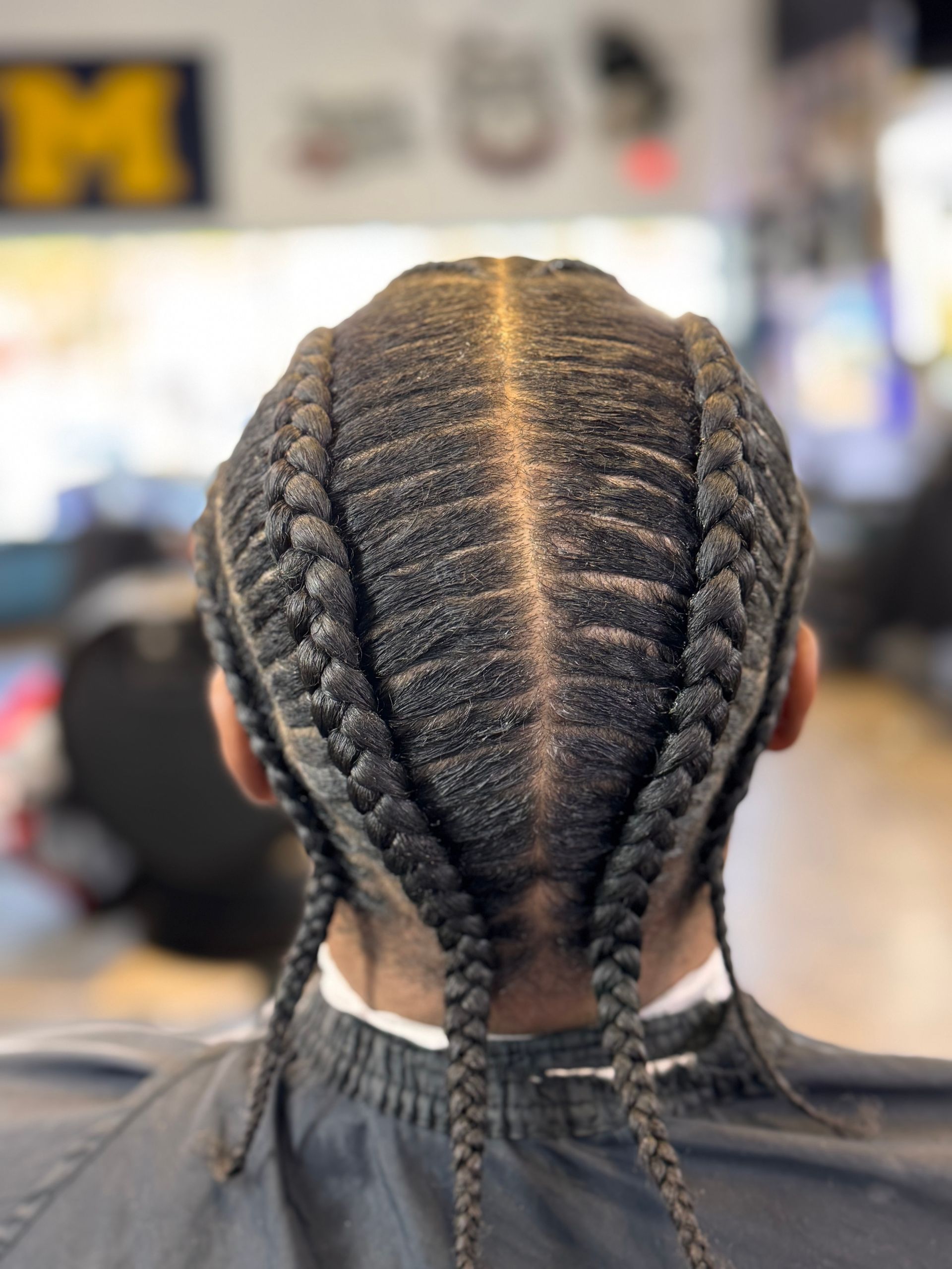 The back of a person 's head with braids and the letter m in the background