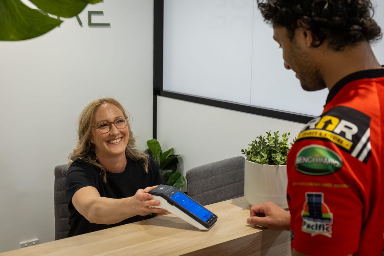 Woman handing payment device to person wearing a red jersey at a counter. Office setting, smiles.