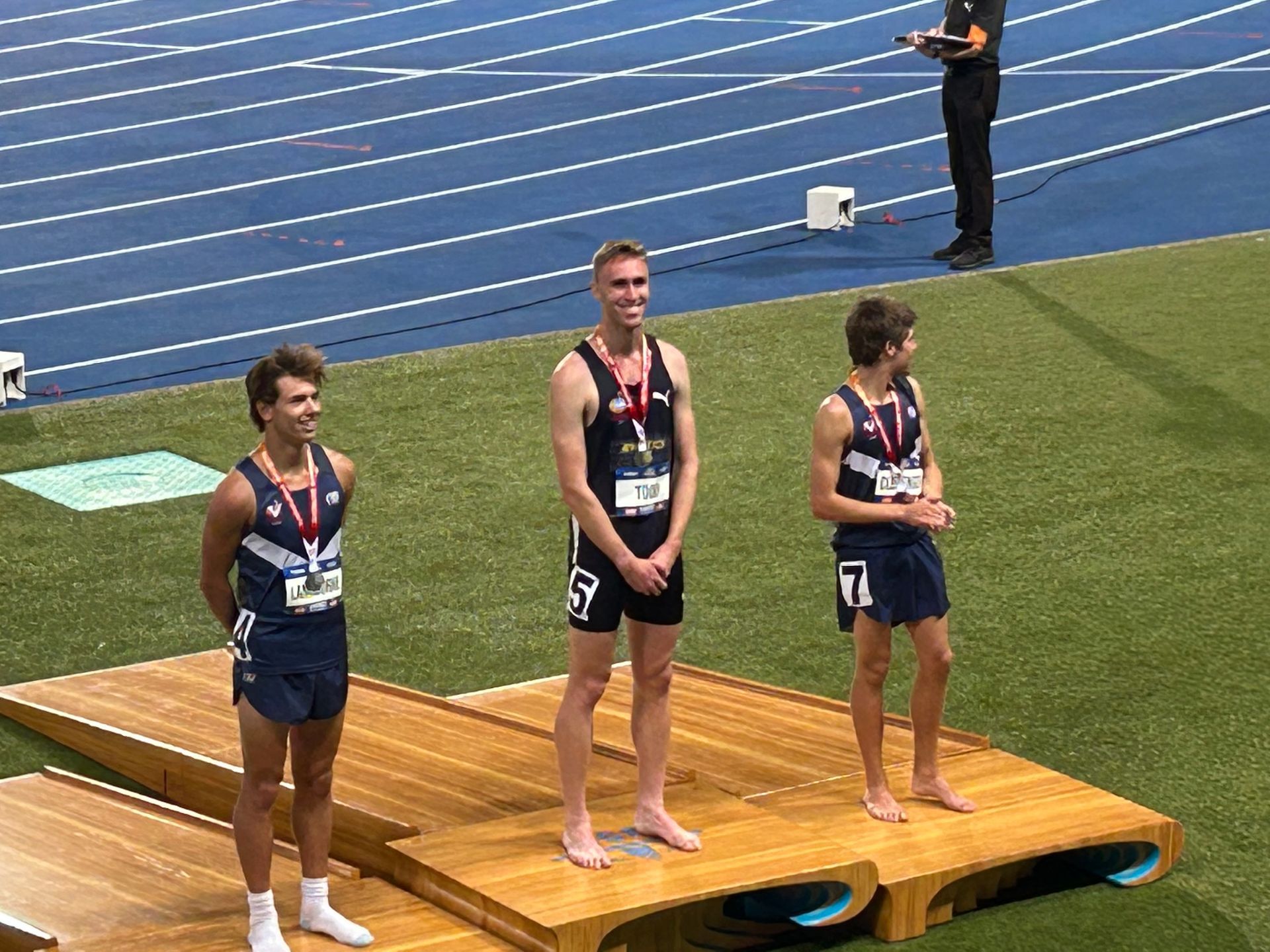 Three men are standing on a wooden podium on a track.