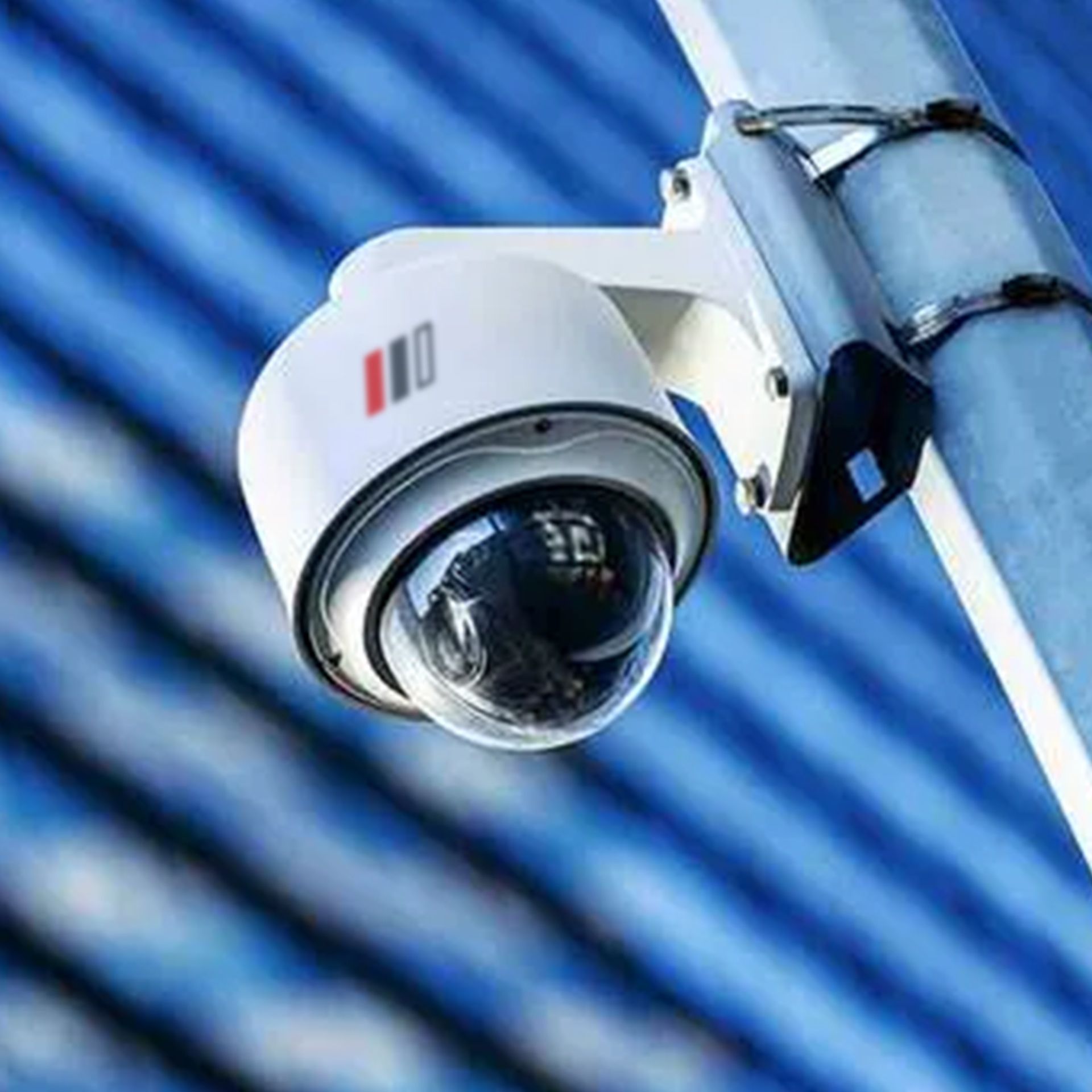 White security camera mounted on a pole, against a blue blurred background.