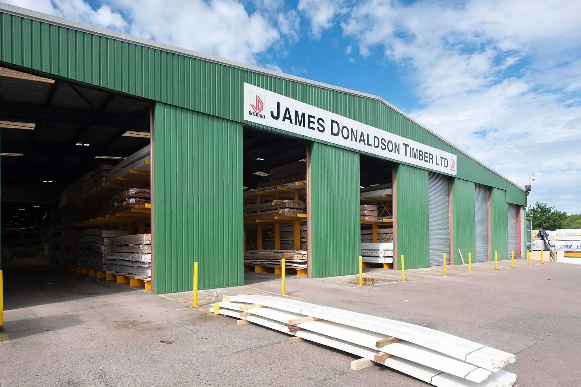 Green warehouse of James Donaldson Timber Ltd, holding stacked lumber.