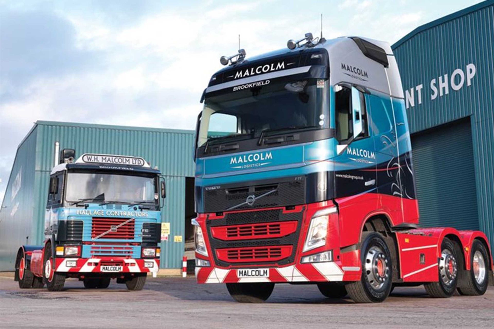 Two Malcolm Freight trucks in front of a building, one old and one modern, both red, blue and white.