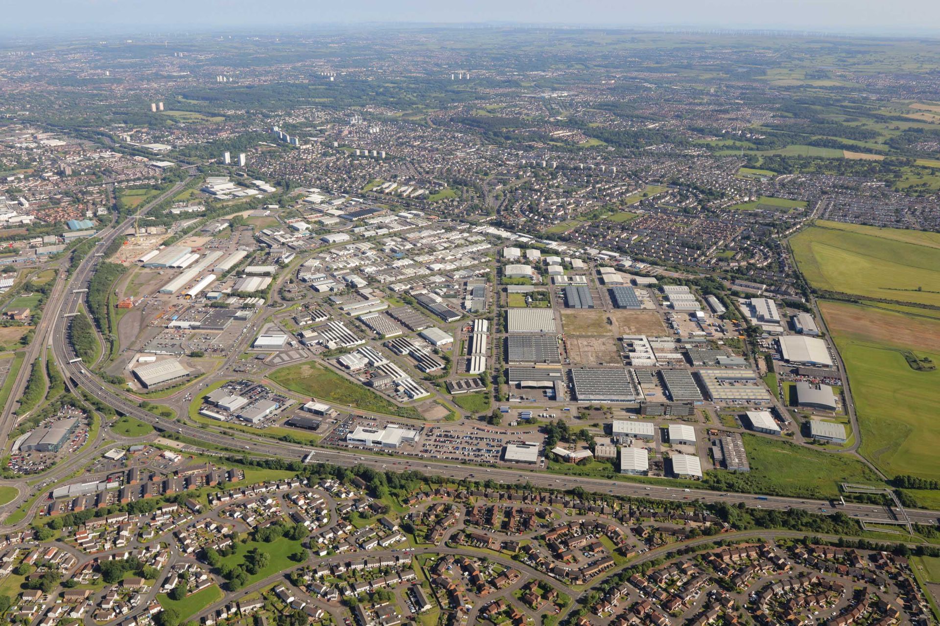 Aerial view of a large industrial area with many buildings, surrounded by residential areas and a highway.