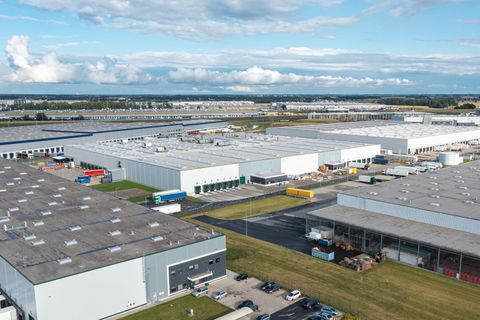 Aerial view of large industrial warehouses with loading docks and parking lots under a cloudy sky.