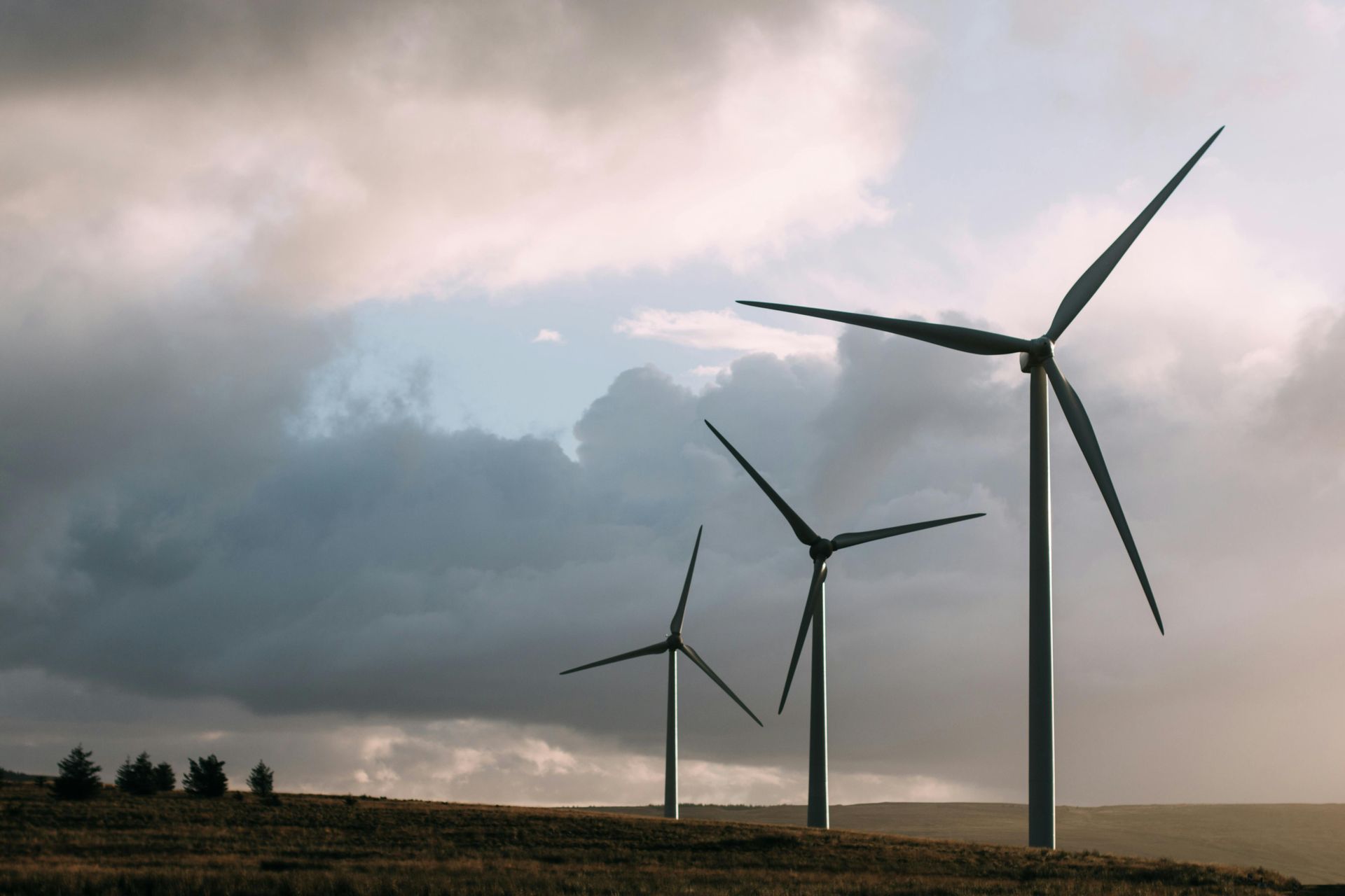 Three wind turbines on a grassy hill under a cloudy sky, generating renewable energy.