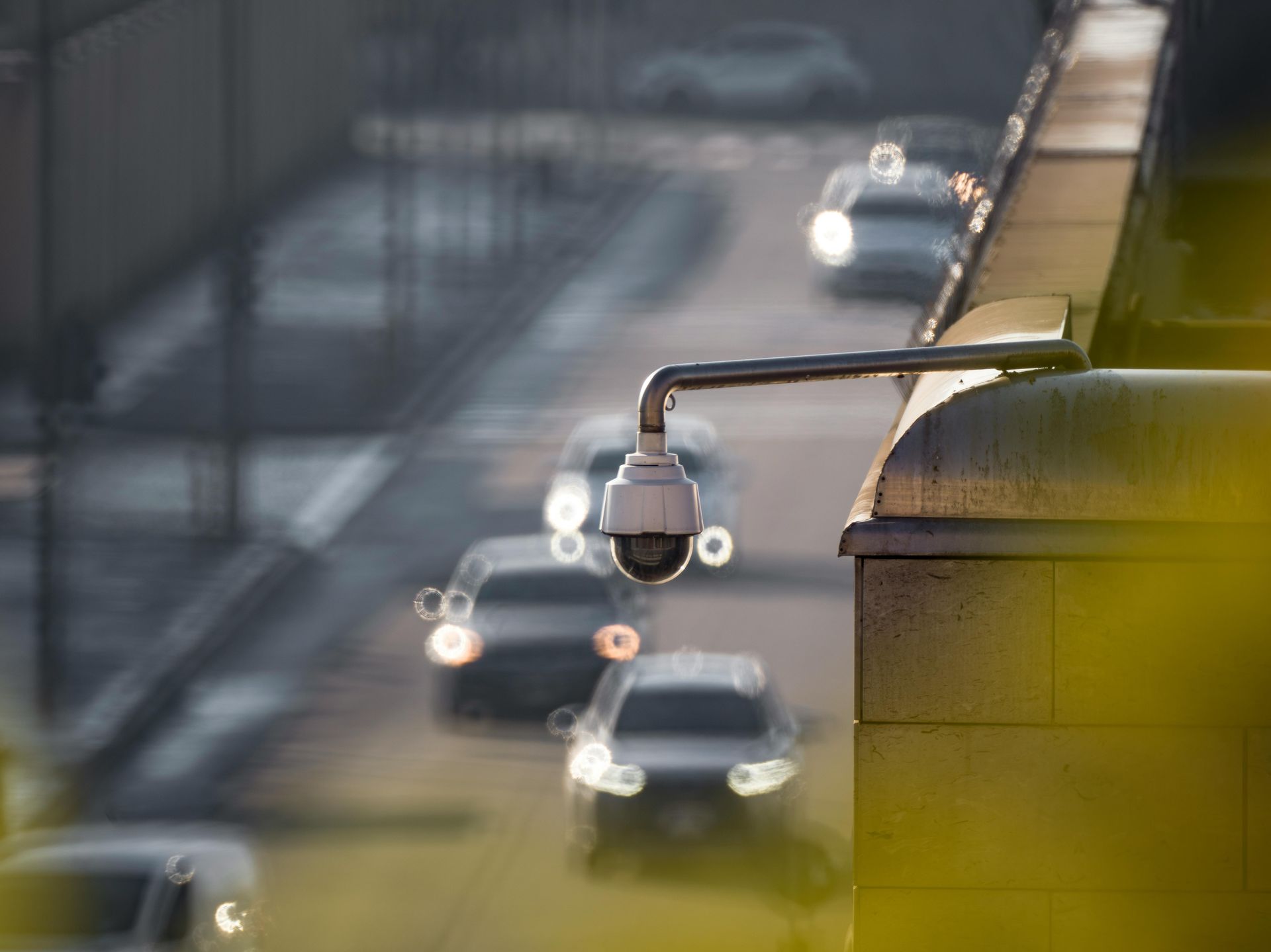 Security camera mounted on a bridge overlooking a busy road with cars, daytime.