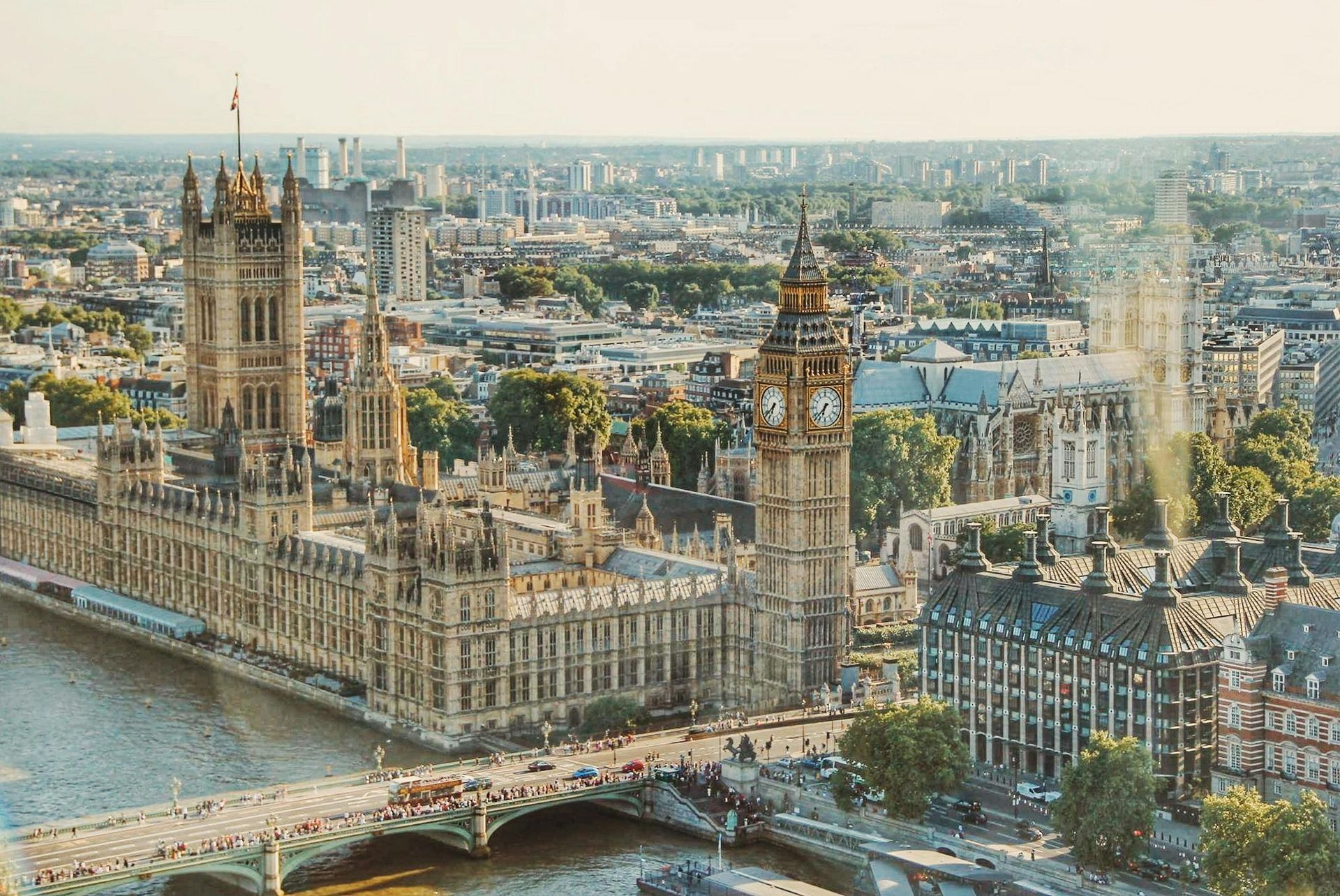 Aerial view of London: Palace of Westminster and Big Ben, sunny day, bridge in foreground, city backdrop.