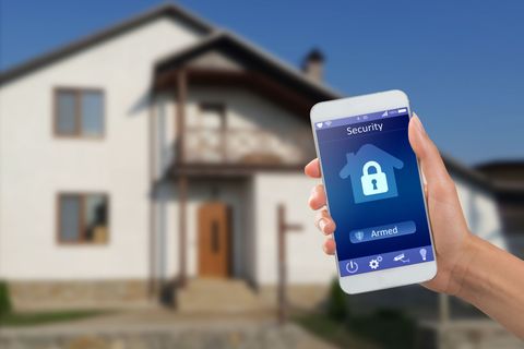 Hand holding smartphone with home security app in front of a house.
