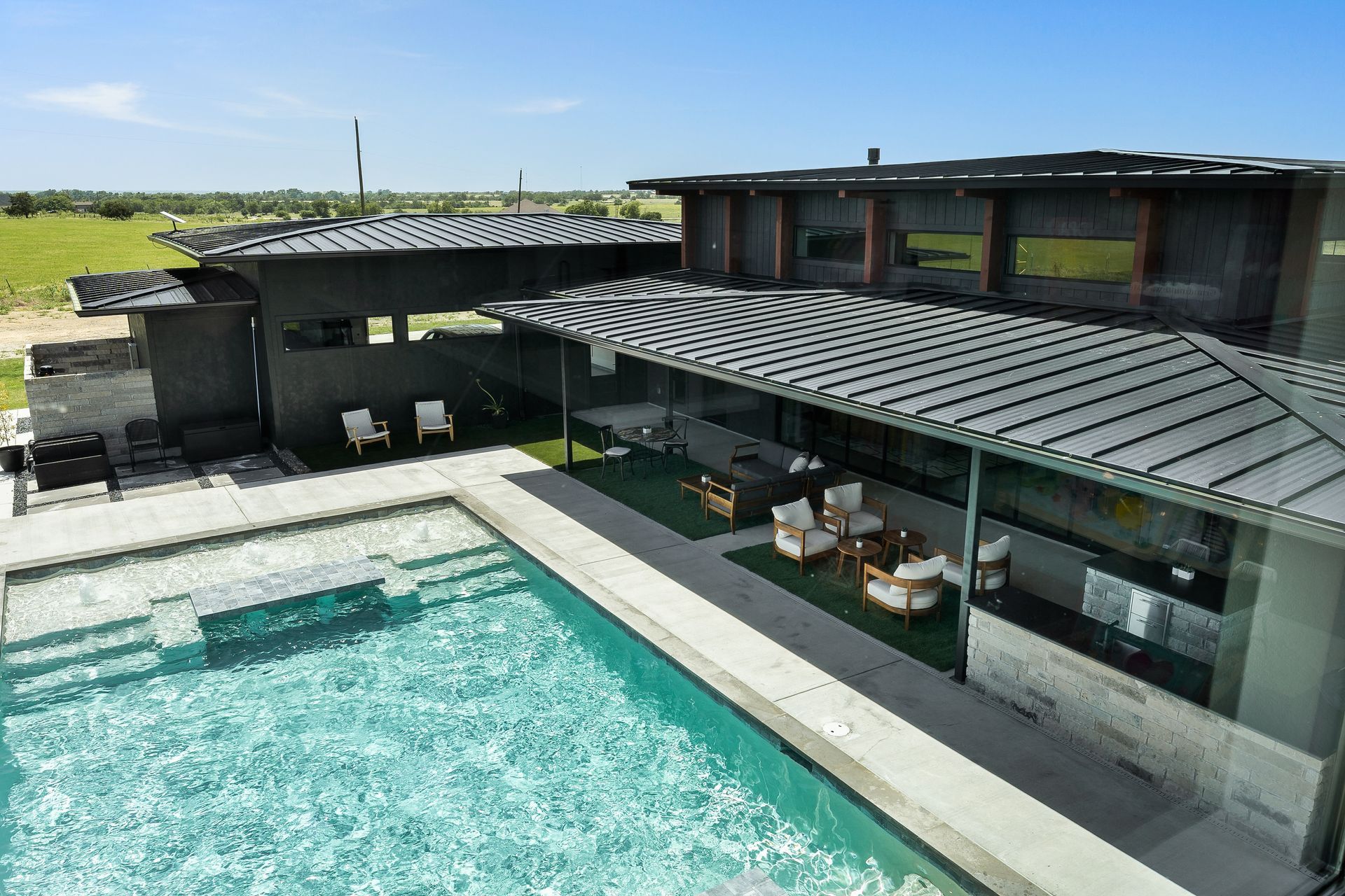 Modern house with a pool and patio seating under a green metal roof
