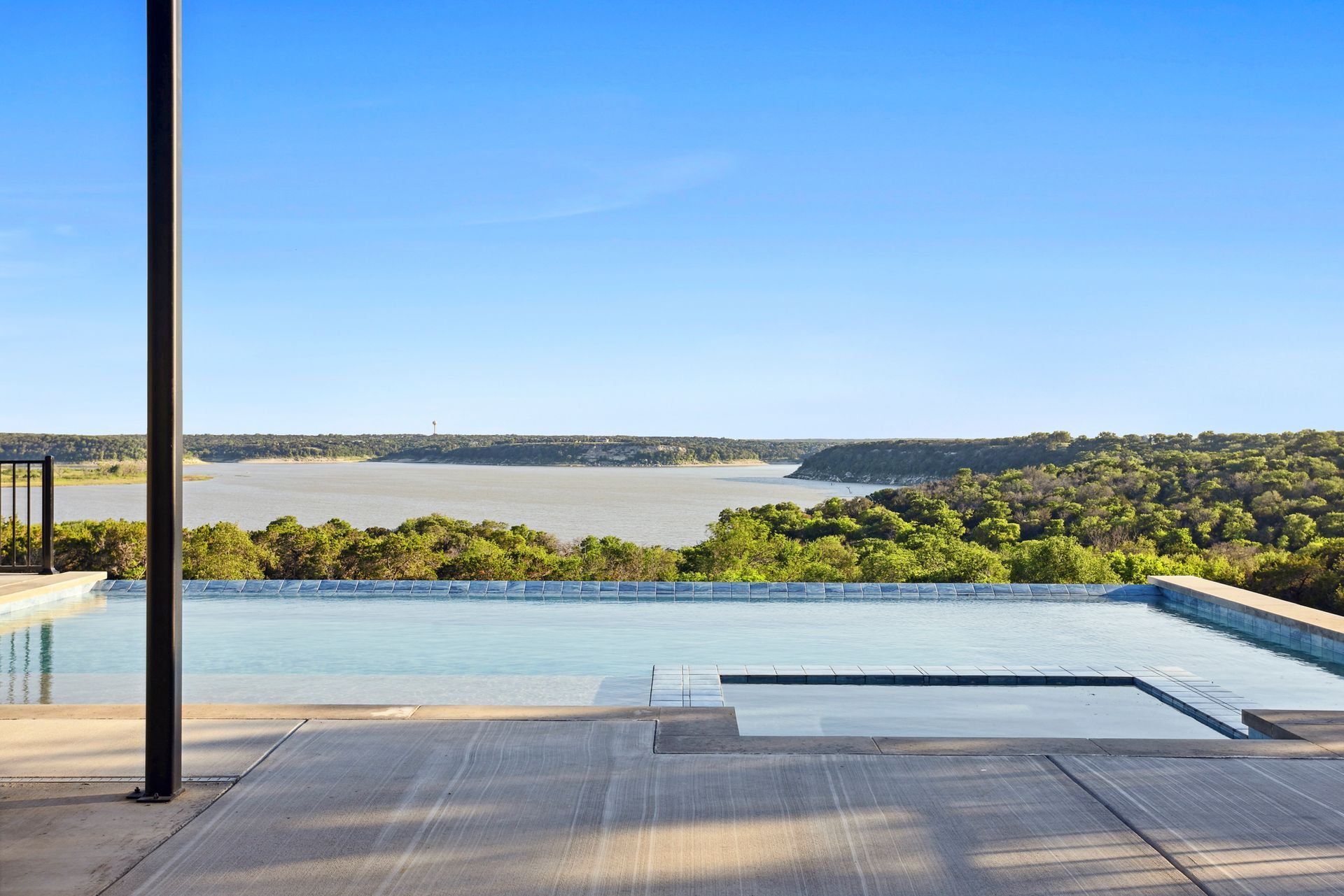 Infinity pool overlooking a lake and green hills under a clear blue sky