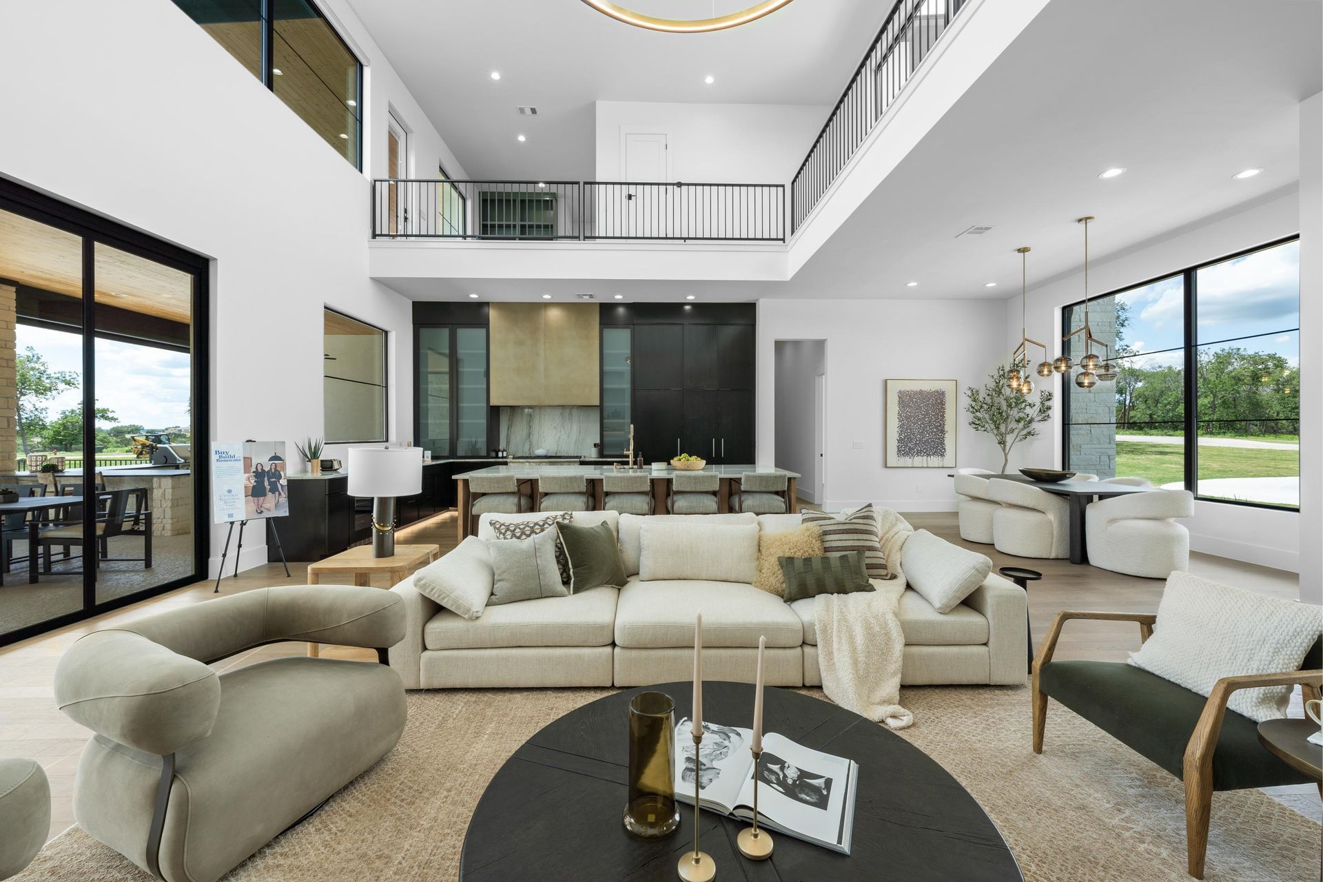 Modern open-plan living room with white sectional sofas, black coffee table, and large windows overlooking greenery
