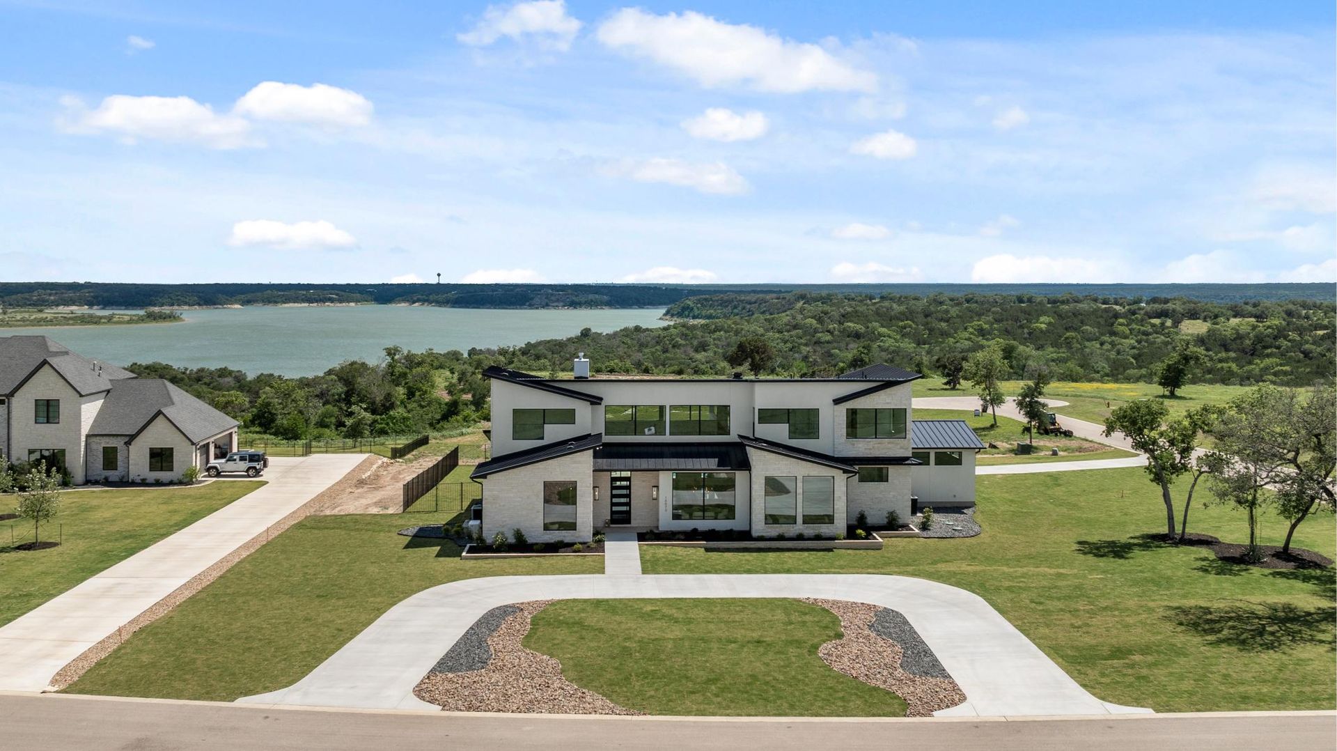 Modern two-story house on a green lakeside property with a wide driveway and scenic water view
