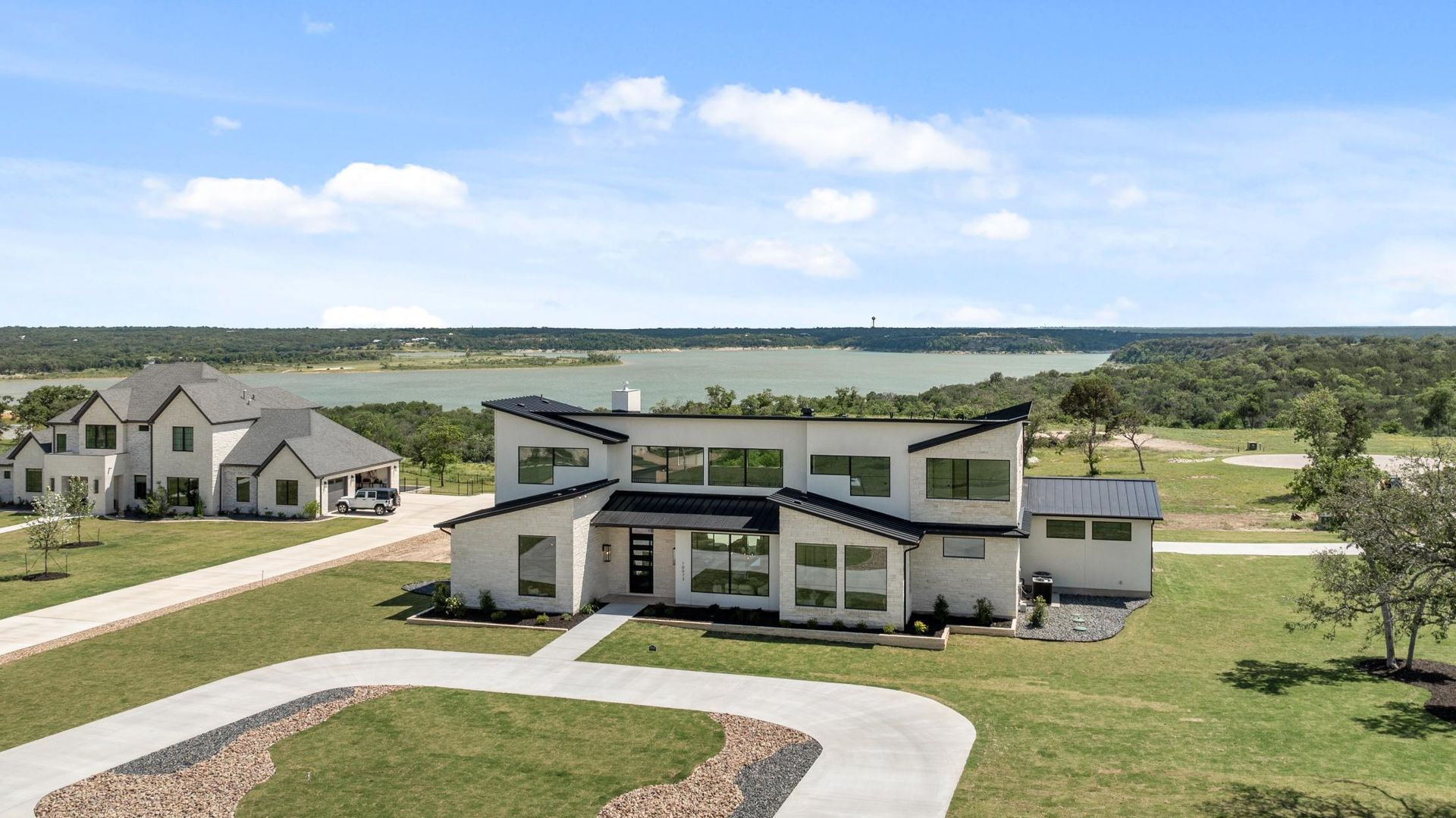 Modern suburban house with white exterior, large windows, and a curved driveway in a grassy neighborhood