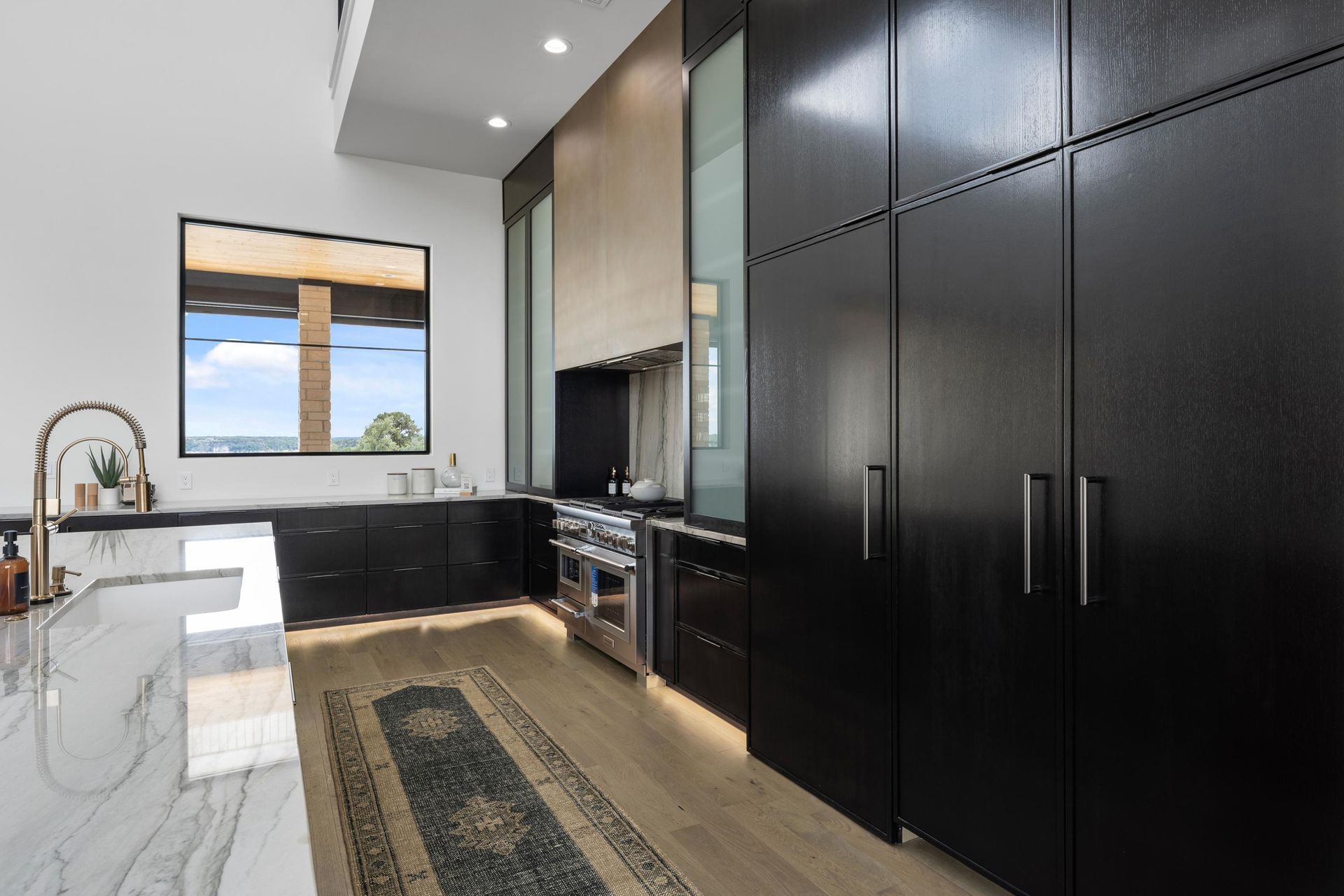 Modern kitchen with black cabinets, white island, and large window overlooking water and sky