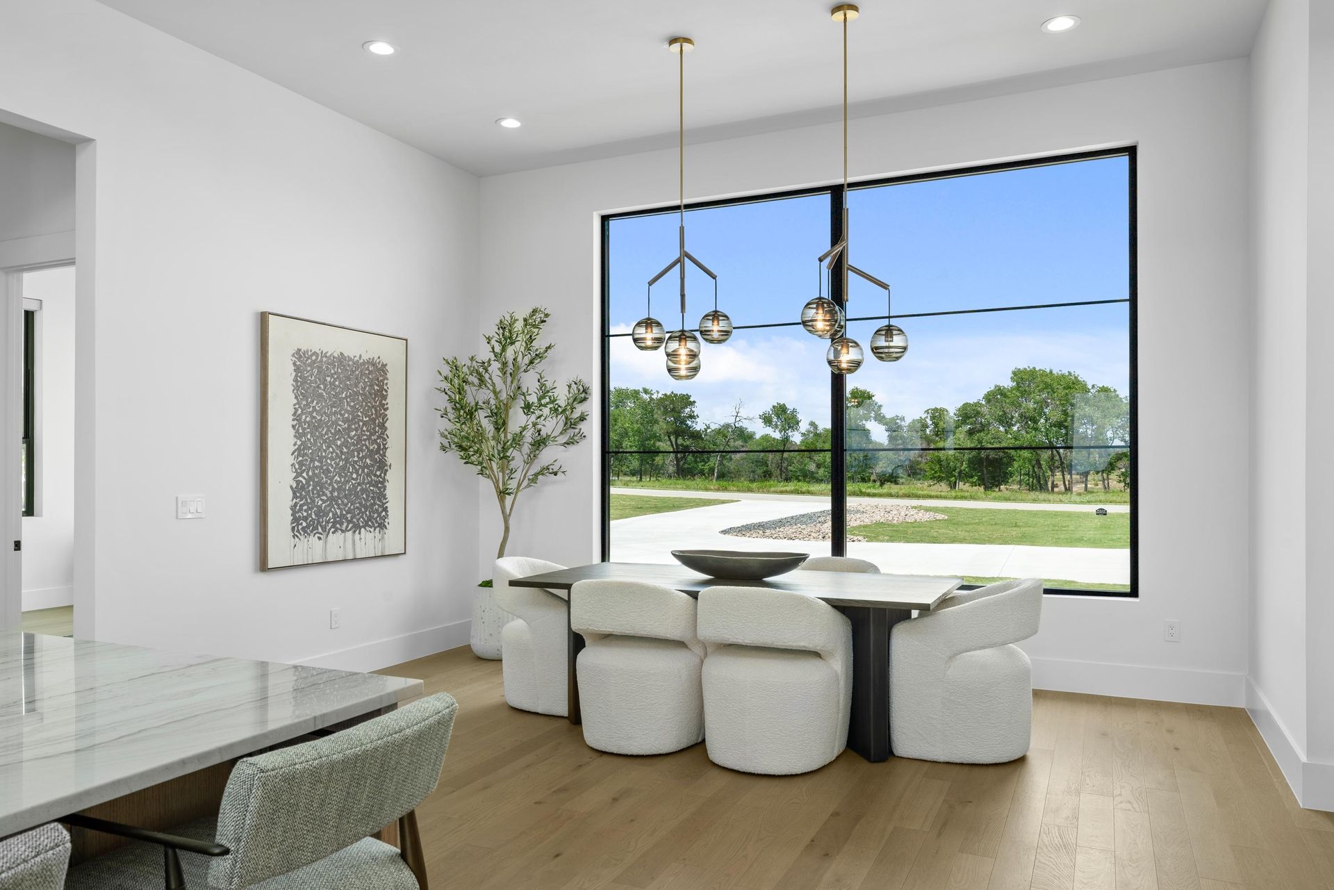 Bright modern dining room with white chairs, large window, and a tree outside.