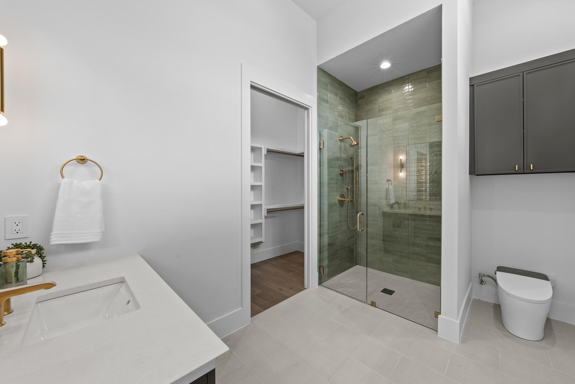 Bright bathroom with glass walk-in shower, white vanity, and gray cabinets