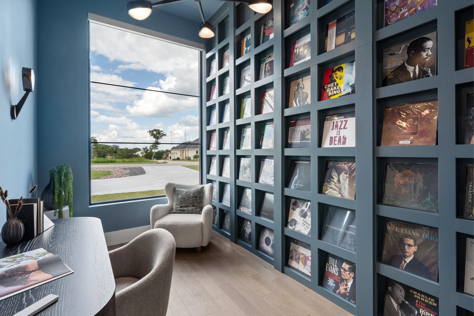 Modern home office with floor-to-ceiling bookshelves, desk, lounge chair, and large window view