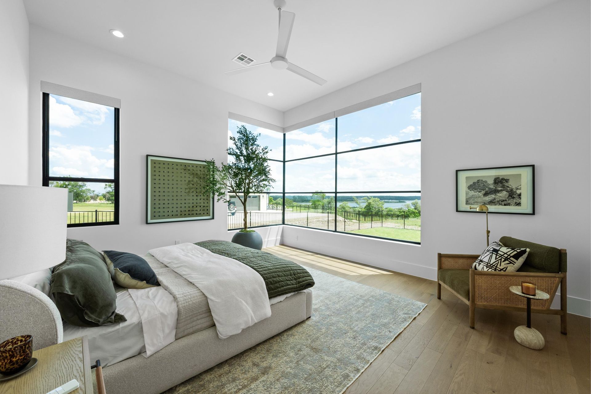 Bright modern bedroom with large corner windows, green accents, and a bed with a view of open fields.
