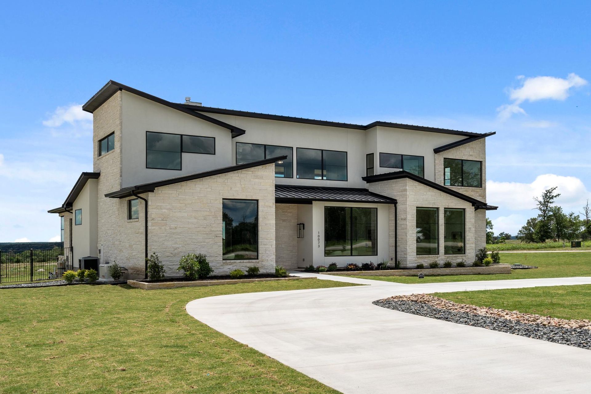 Modern two-story house with beige siding, large windows, and a curved driveway under a blue sky