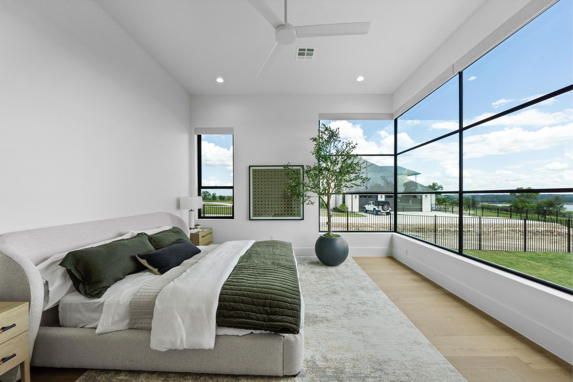 Bright modern bedroom with a bed, large windows, and a balcony view of water and sky